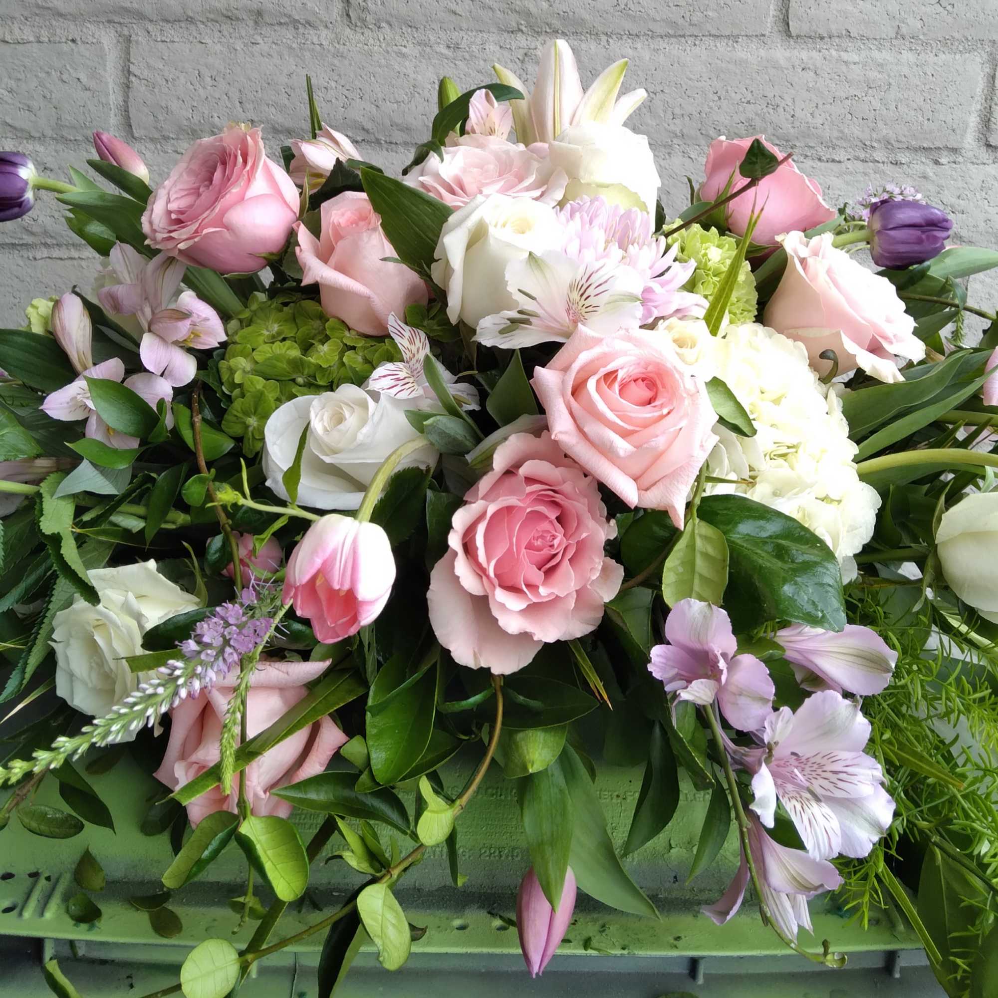 This casket spray is filled with assorted pink seasonal blooms.