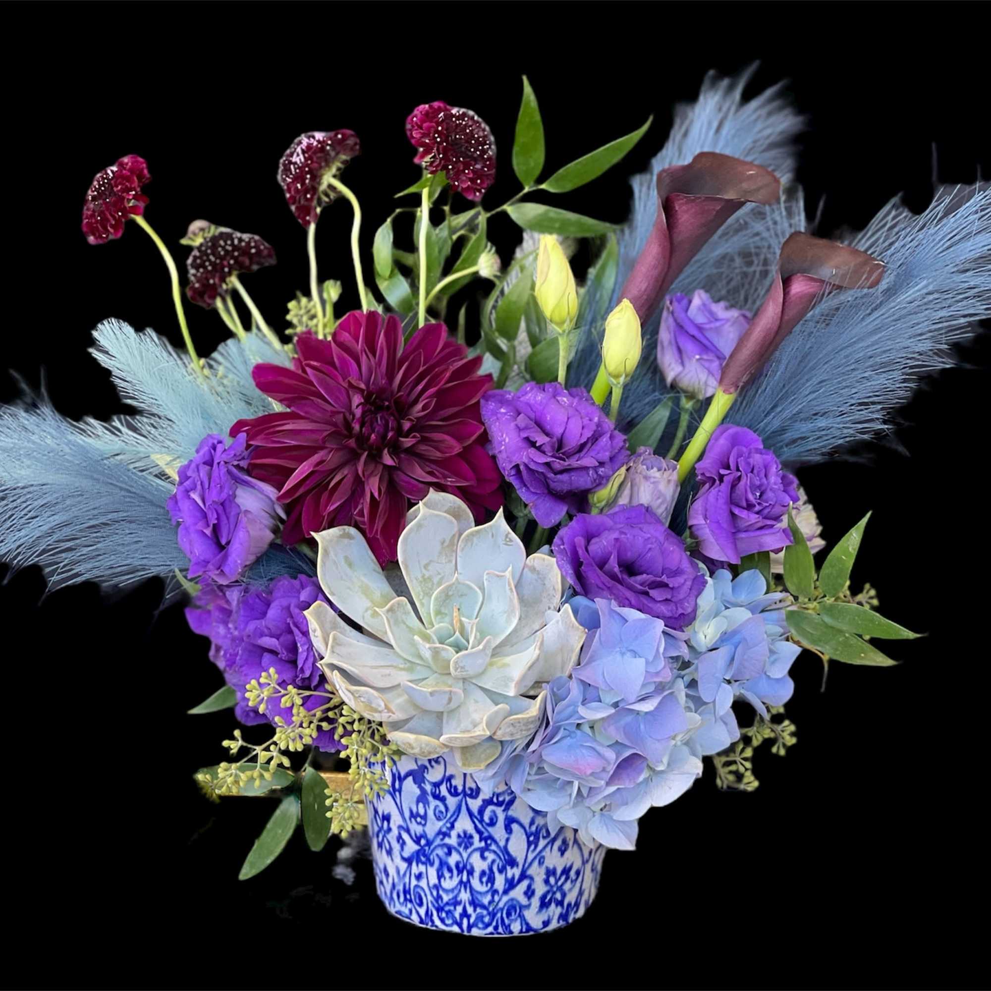 Bright purple, deep red dahlias, and leaves in a decorated ceramic vase.
