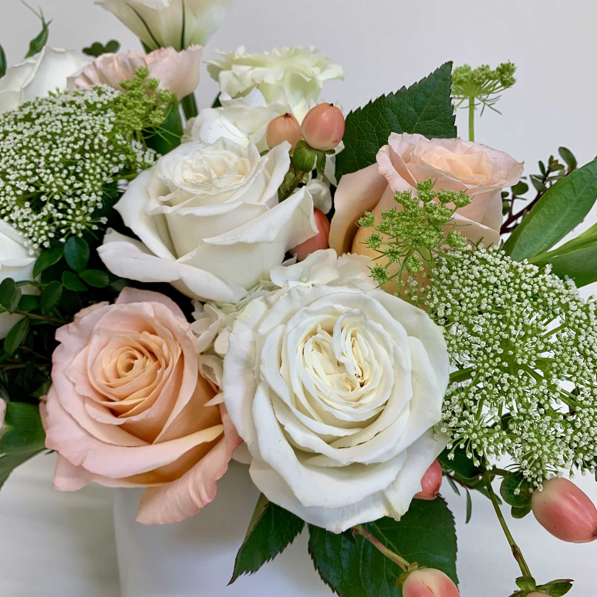 This arrangement features playa blanca and shimmer roses, peach carnations, white lisianthus