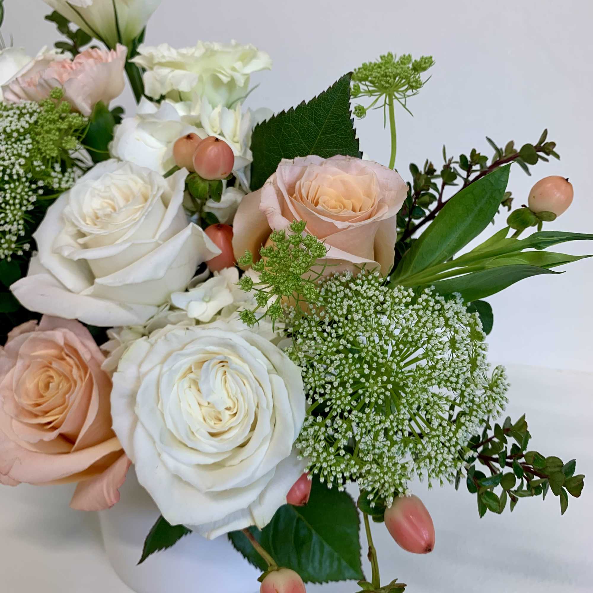 This arrangement features playa blanca and shimmer roses, peach carnations, white lisianthus