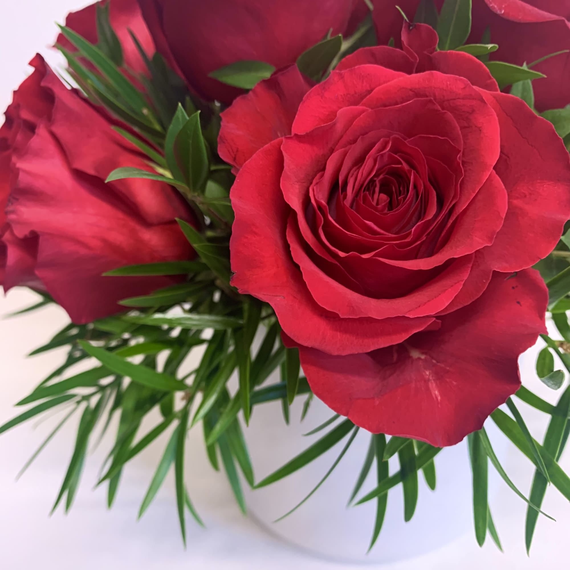 A luscious mix of red roses and greens delivered in a white