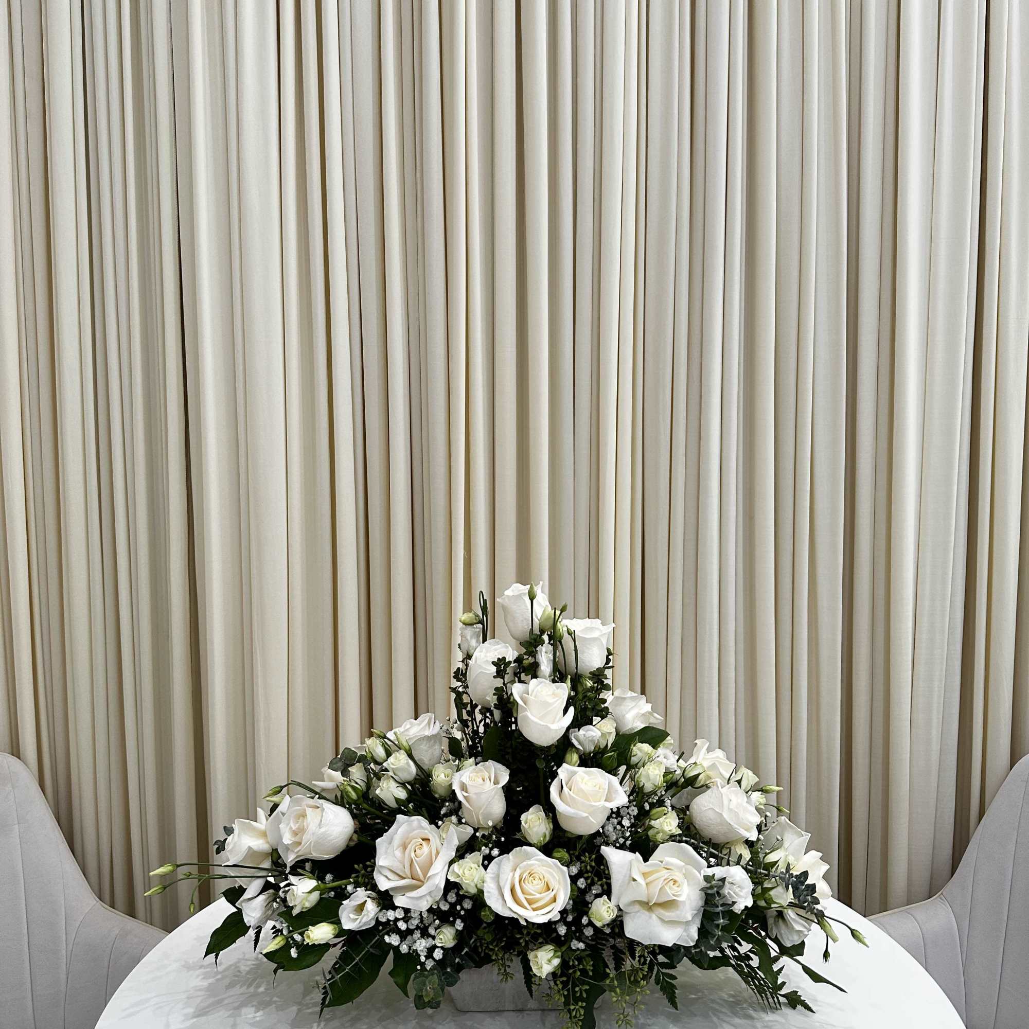 This serene arrangement of white roses and baby roses expresses heartfelt sympathy