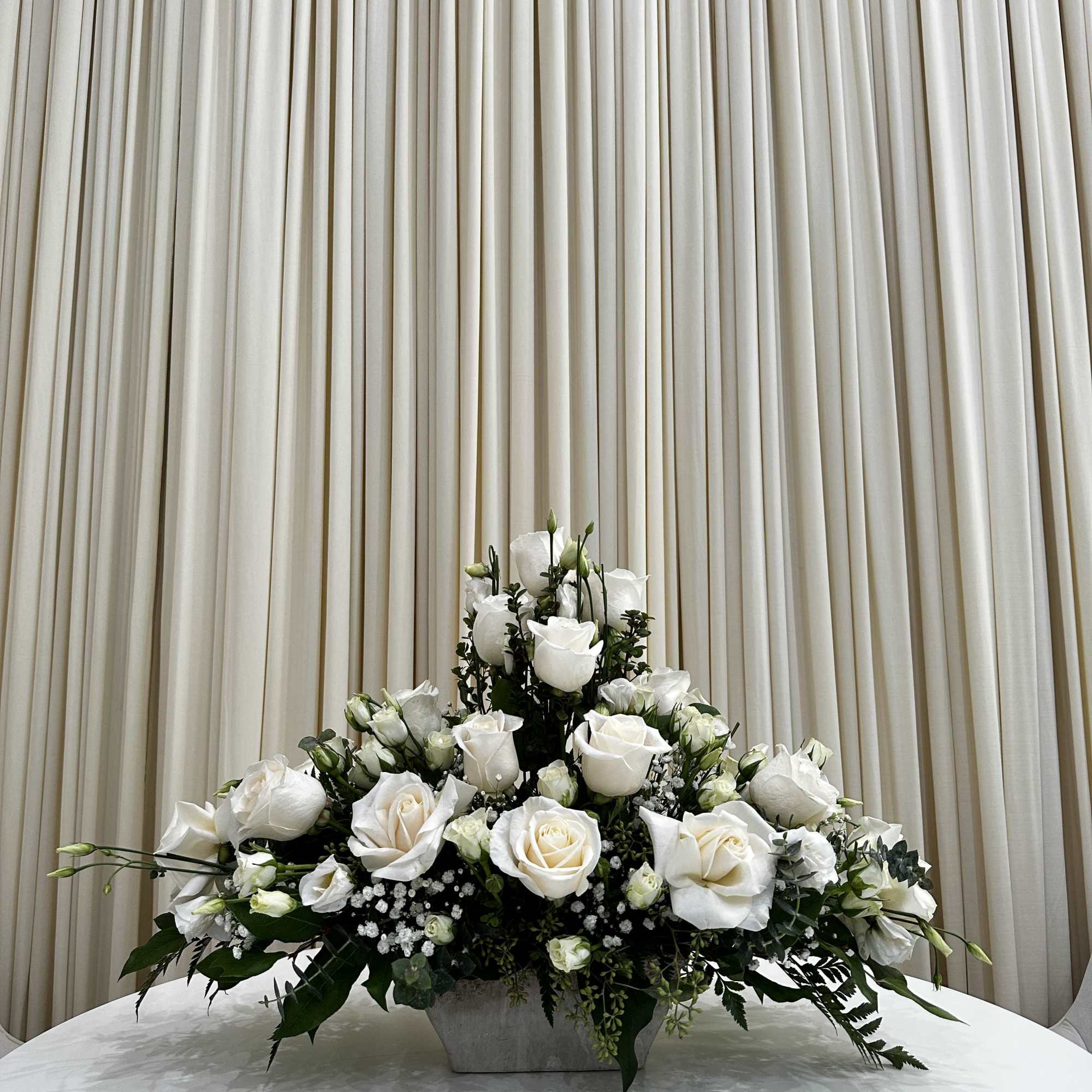 This serene arrangement of white roses and baby roses expresses heartfelt sympathy
