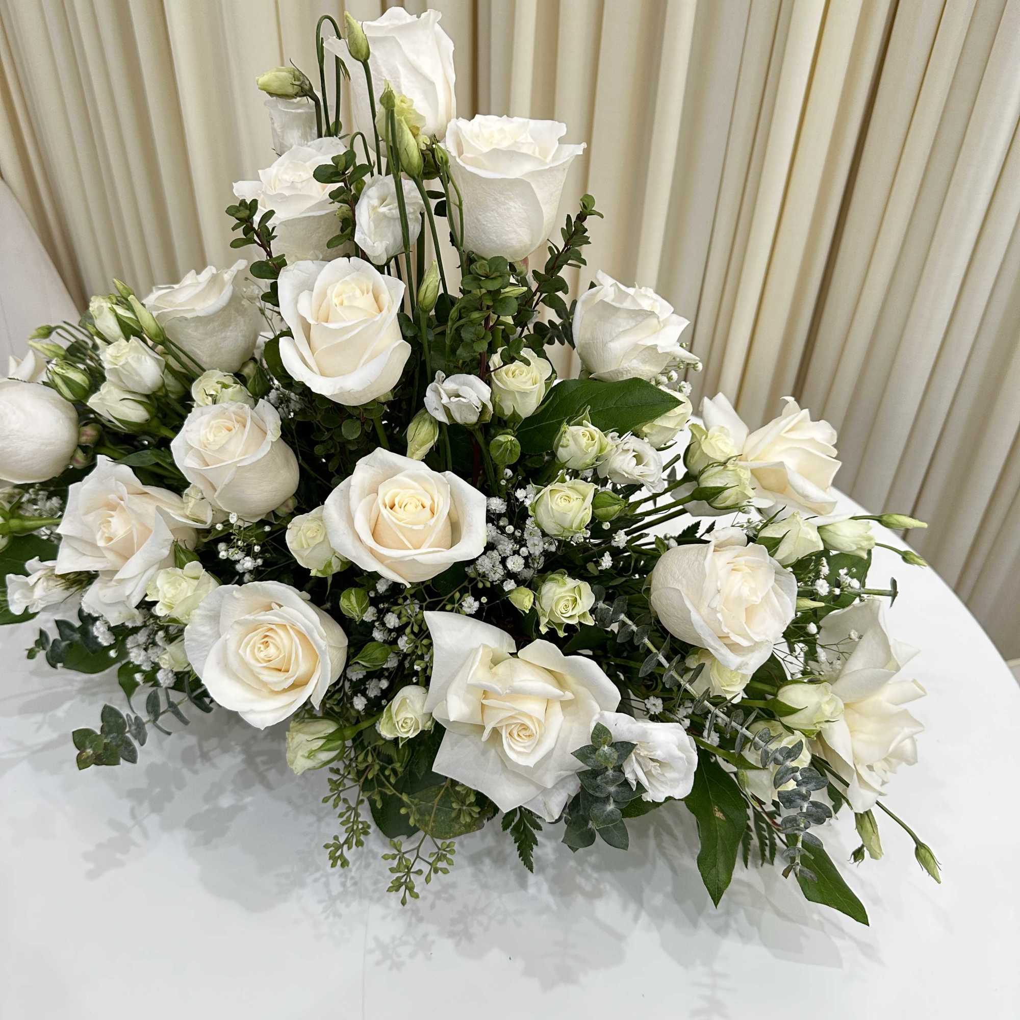 This serene arrangement of white roses and baby roses expresses heartfelt sympathy