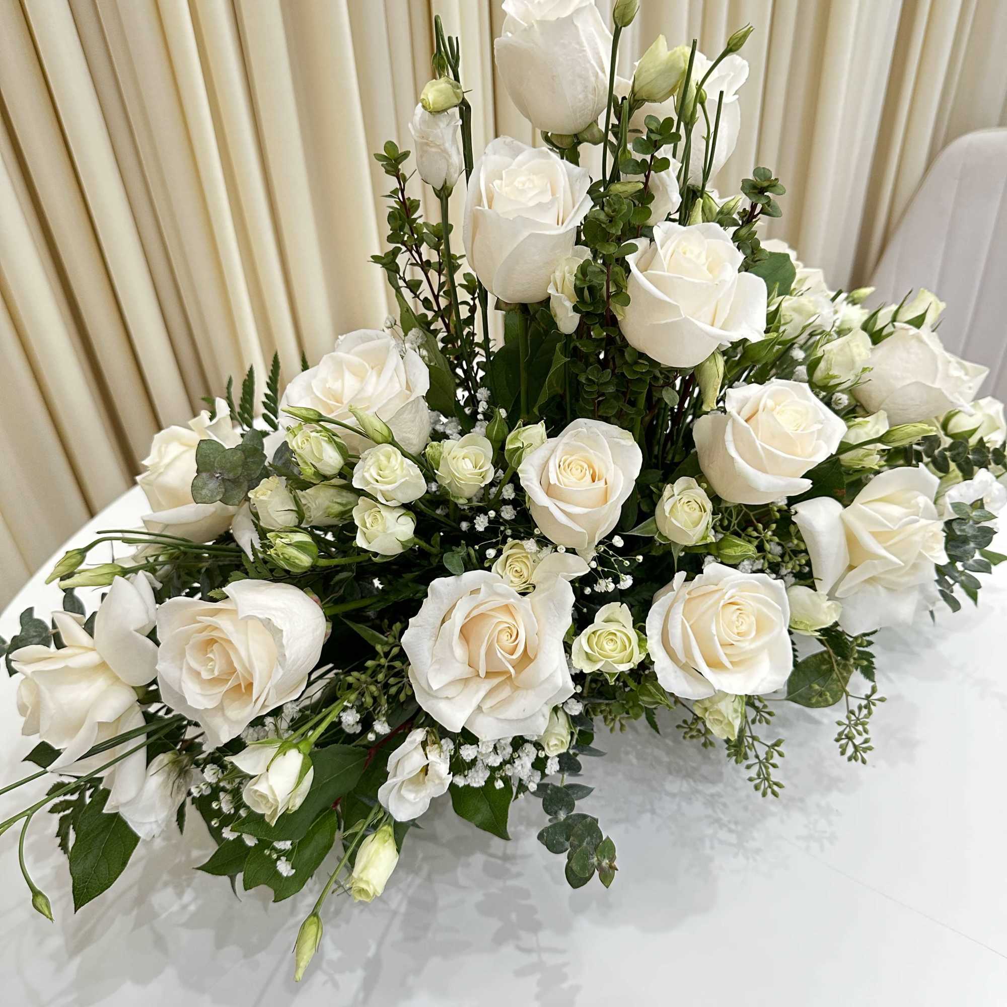 This serene arrangement of white roses and baby roses expresses heartfelt sympathy
