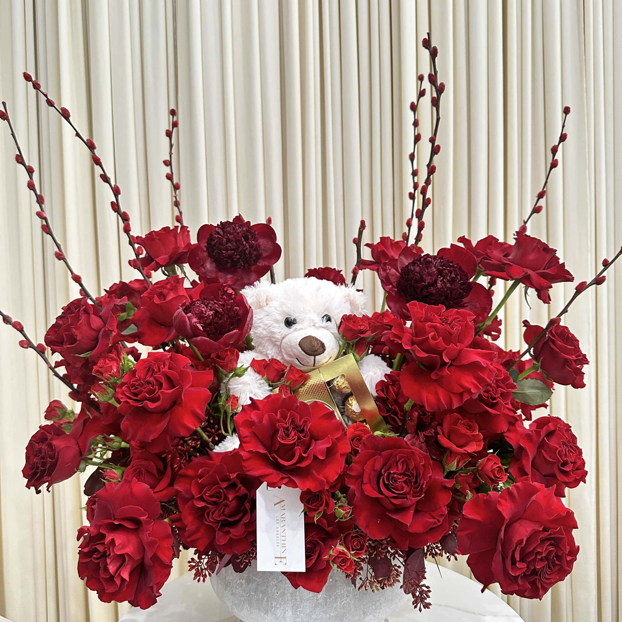 This delightful arrangement features a cuddly white teddy bear nestled amidst a