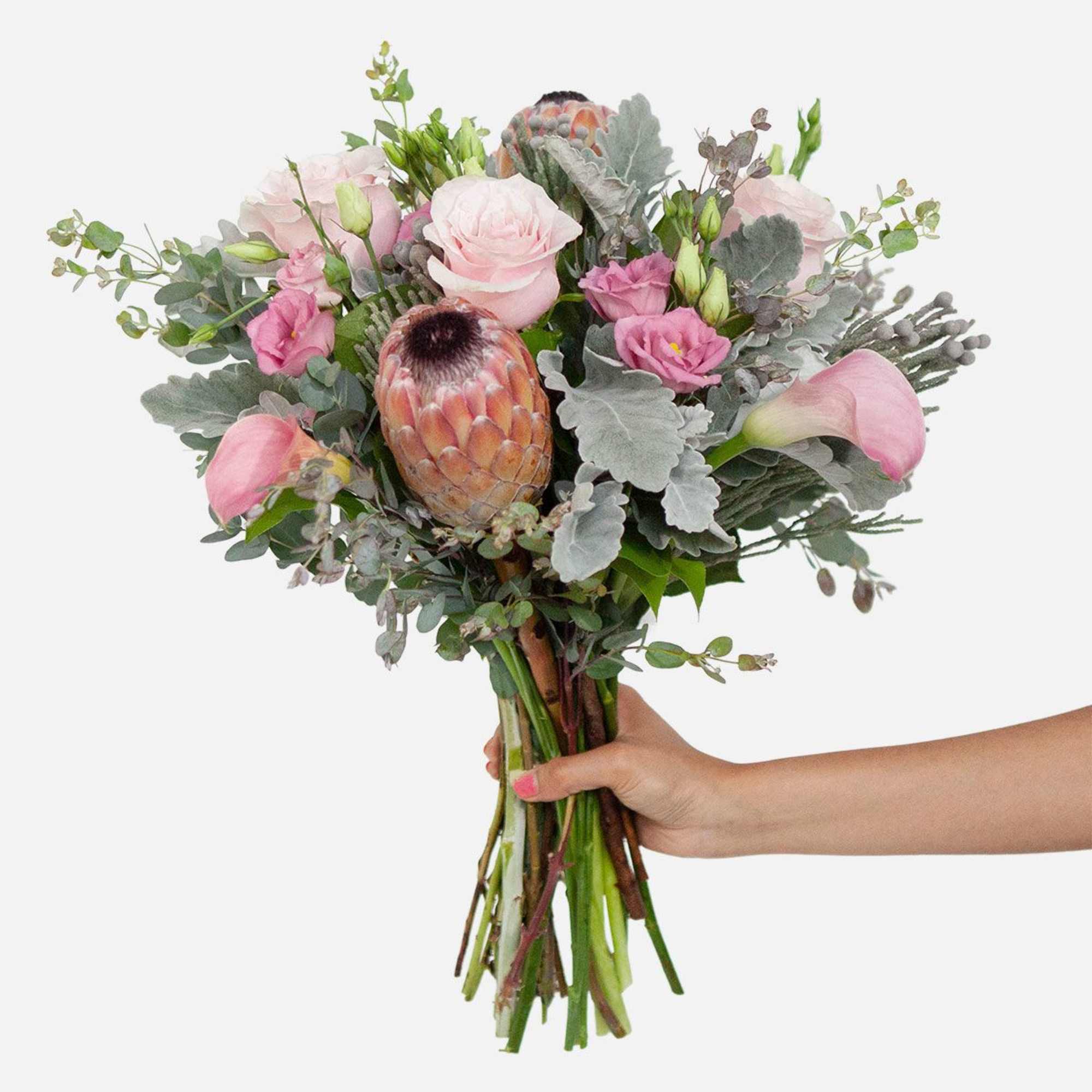A handcrafted bouquet of blush pink roses, calla lilies, lisianthis, and protea