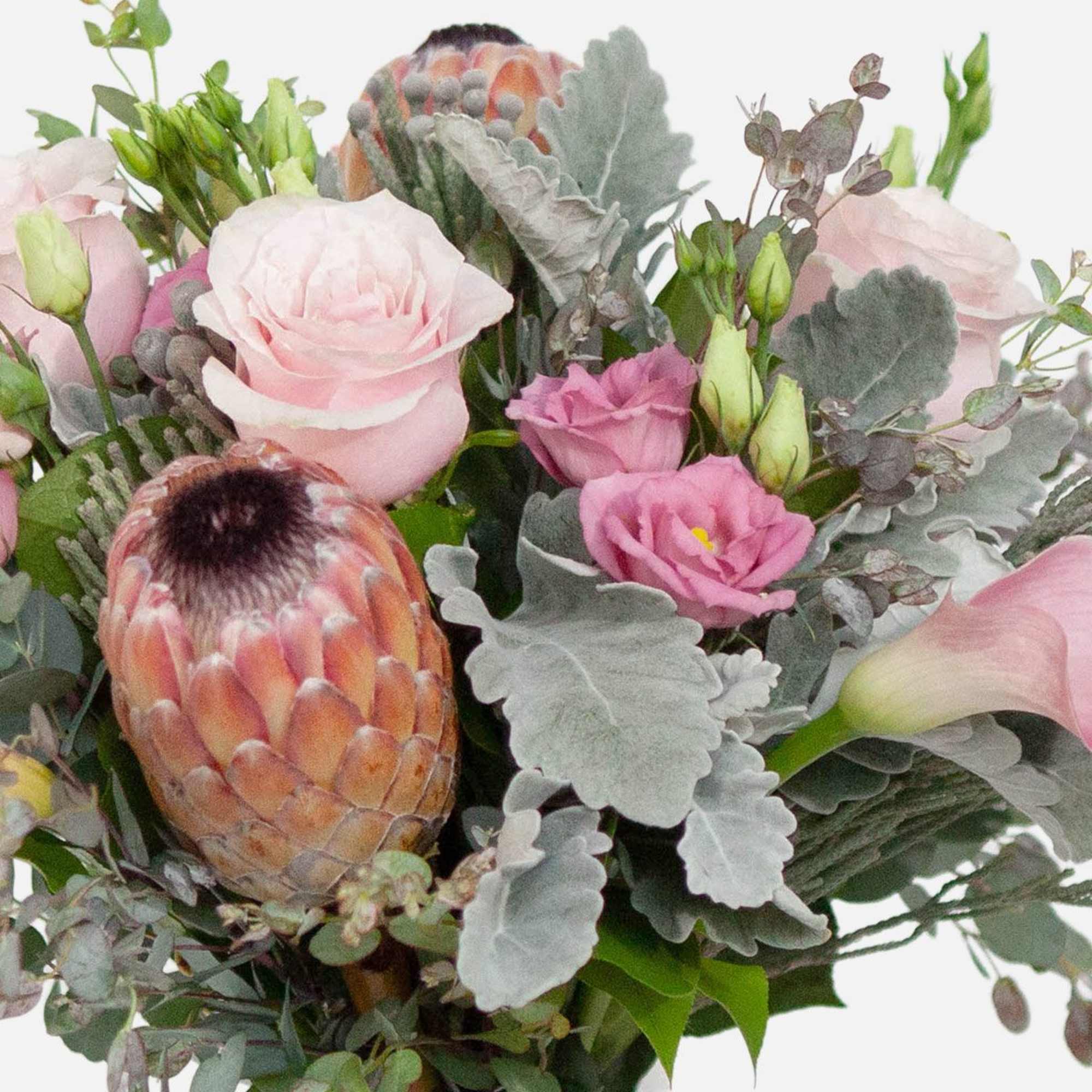 A handcrafted bouquet of blush pink roses, calla lilies, lisianthis, and protea