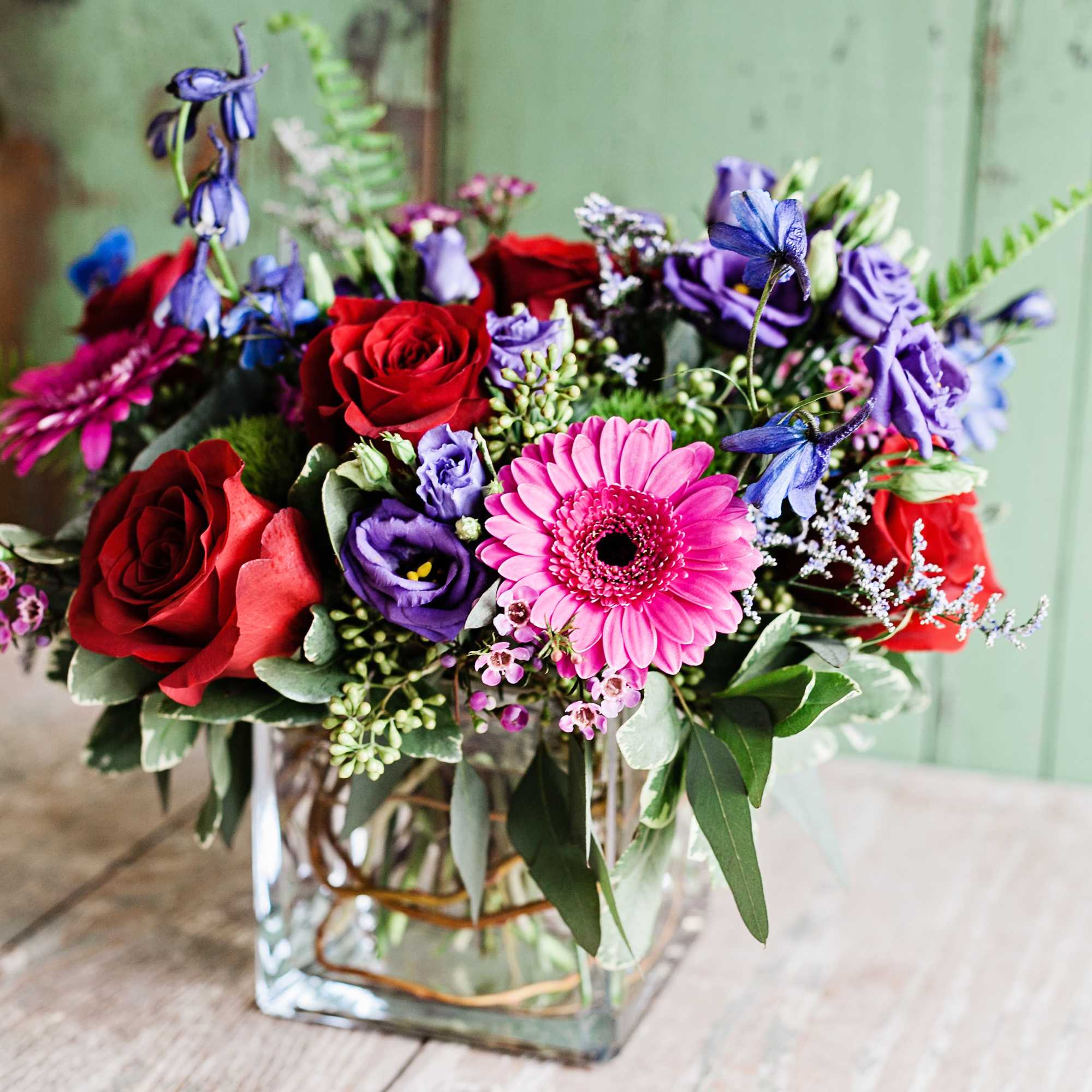 Jewel toned flowers designed in a glass cube lined with curly willow. Jewel toned flowers designed in a glass cube lined with curly willow.