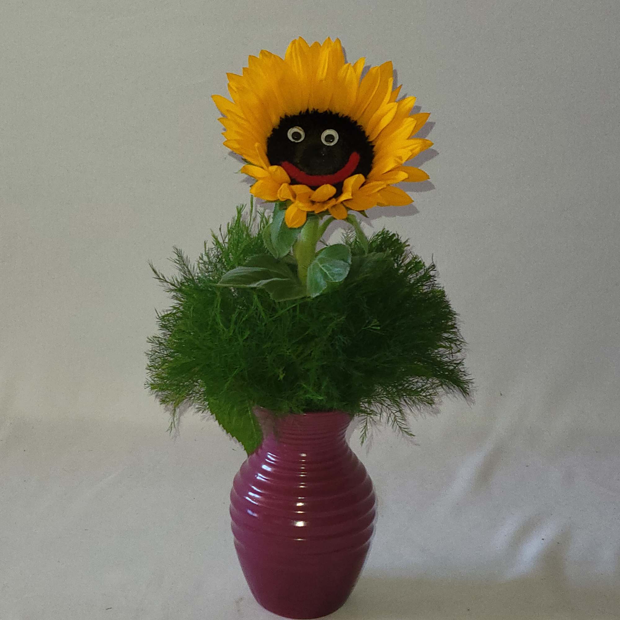 Sunflower with smiley face, tree fern and small vase. Colors of the