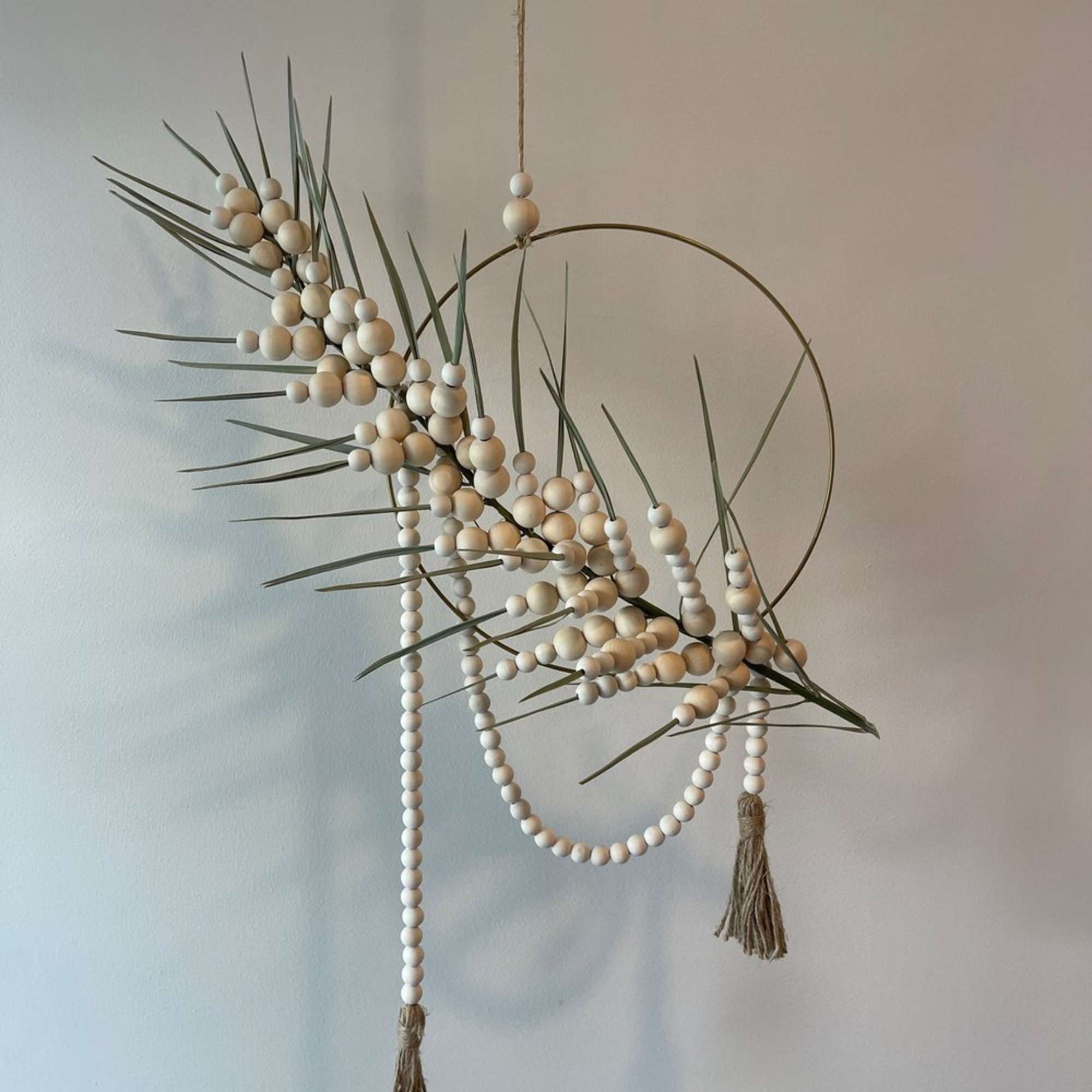 - Circular hanging floral arrangement with graceful palm frond
- Intertwined with delicate