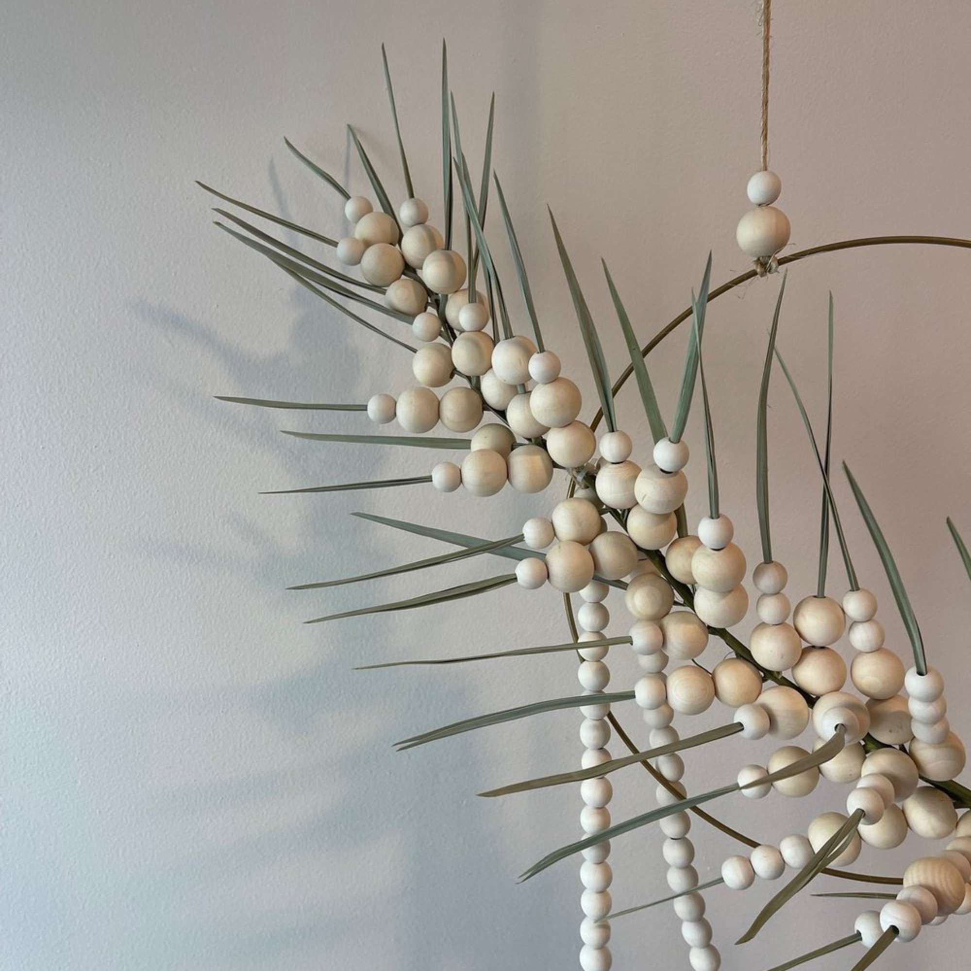 - Circular hanging floral arrangement with graceful palm frond
- Intertwined with delicate