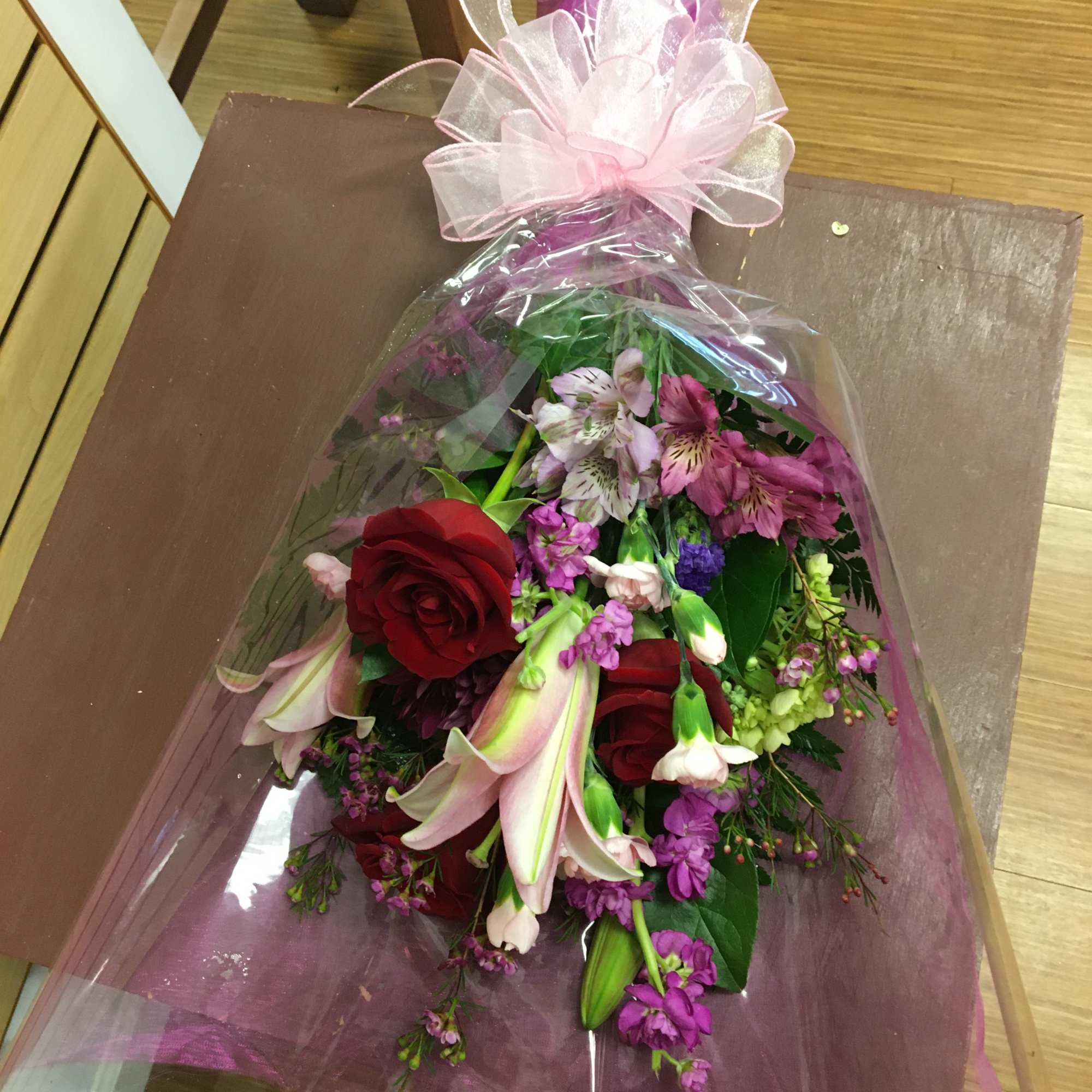 Mixed cut wrapped with a bow. Pictured has red roses, pink lilies Mixed cut wrapped with a bow. Pictured has red roses, pink lilies