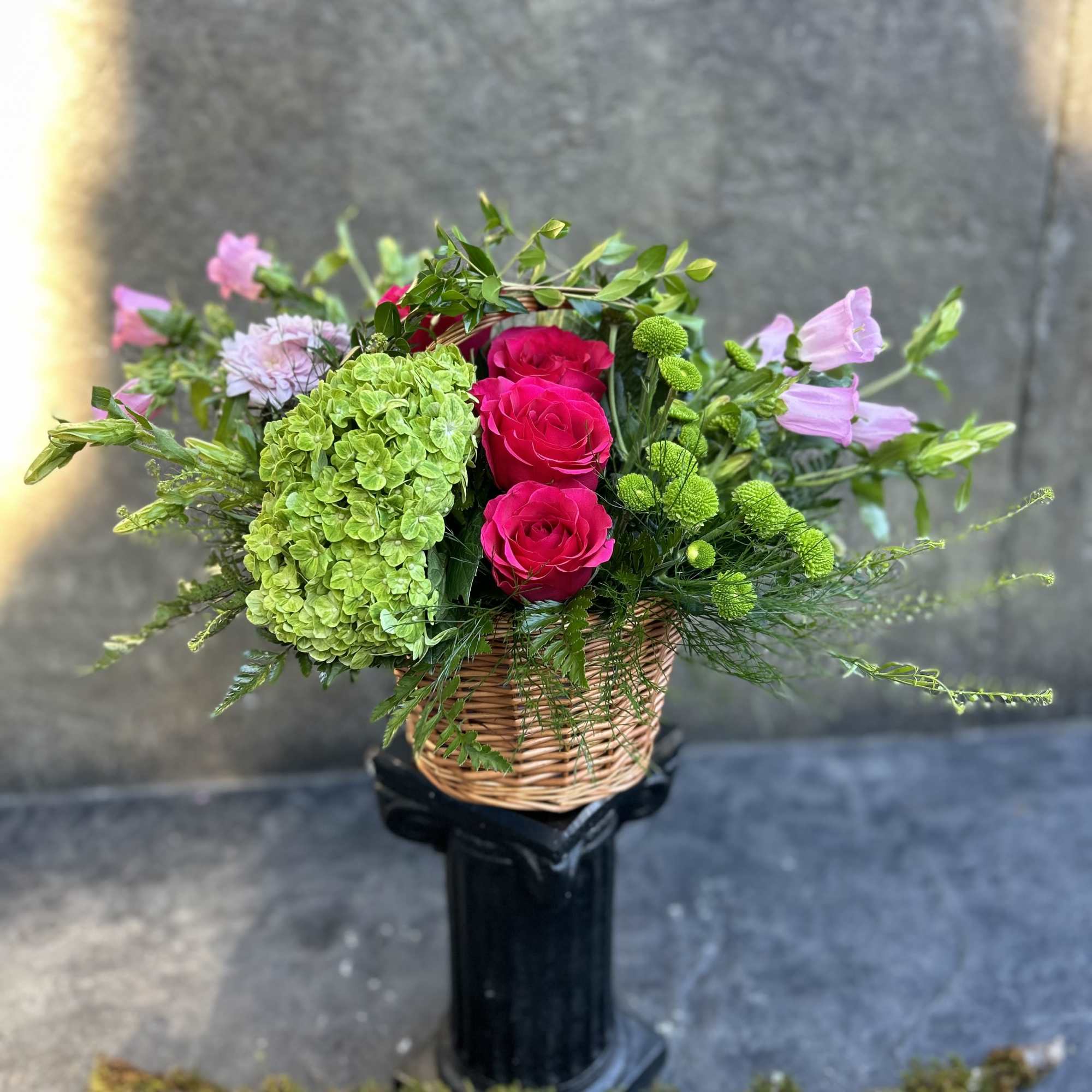 A green basket with a pop of hot pink roses, this arrangement