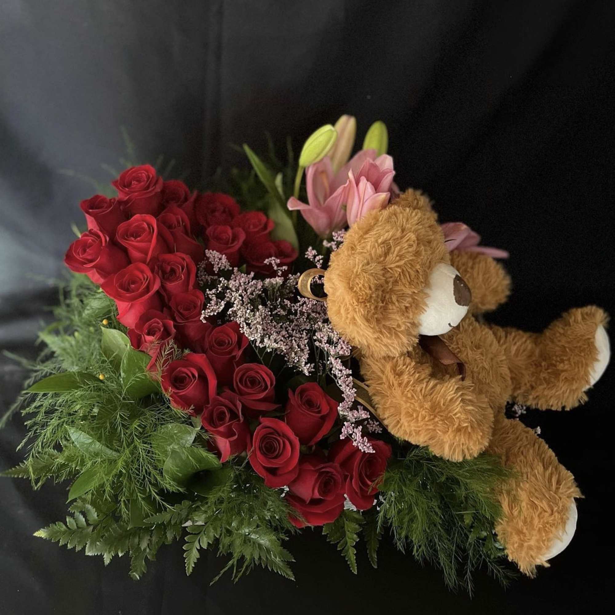 A dozen roses, lilies, with limonium, green foliage and a teddy bear.