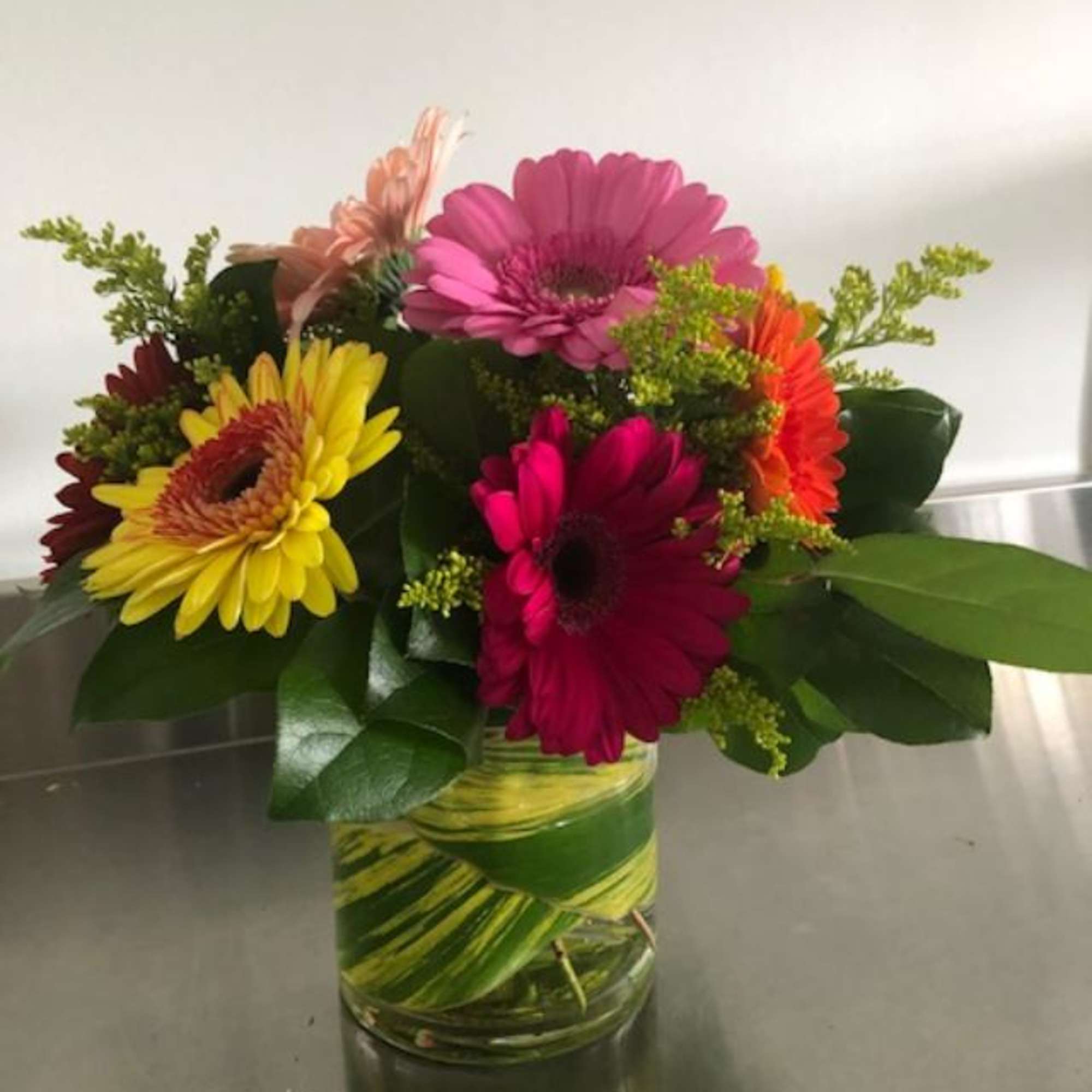 A beautiful display of gerbera daisies in a low cylinder vase. Packs