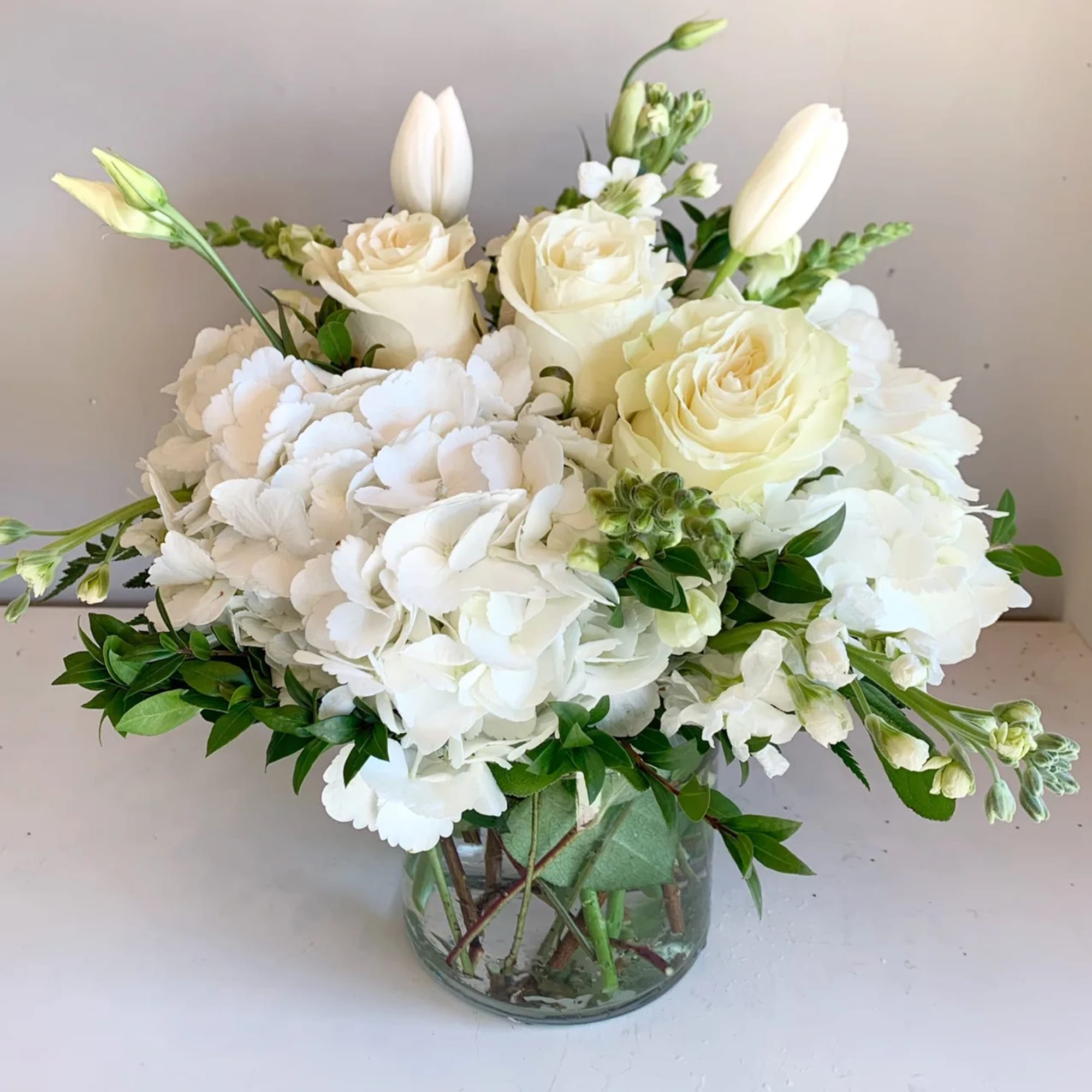 Whites with a touch of greenery in a clear glass vase. Whites with a touch of greenery in a clear glass vase.