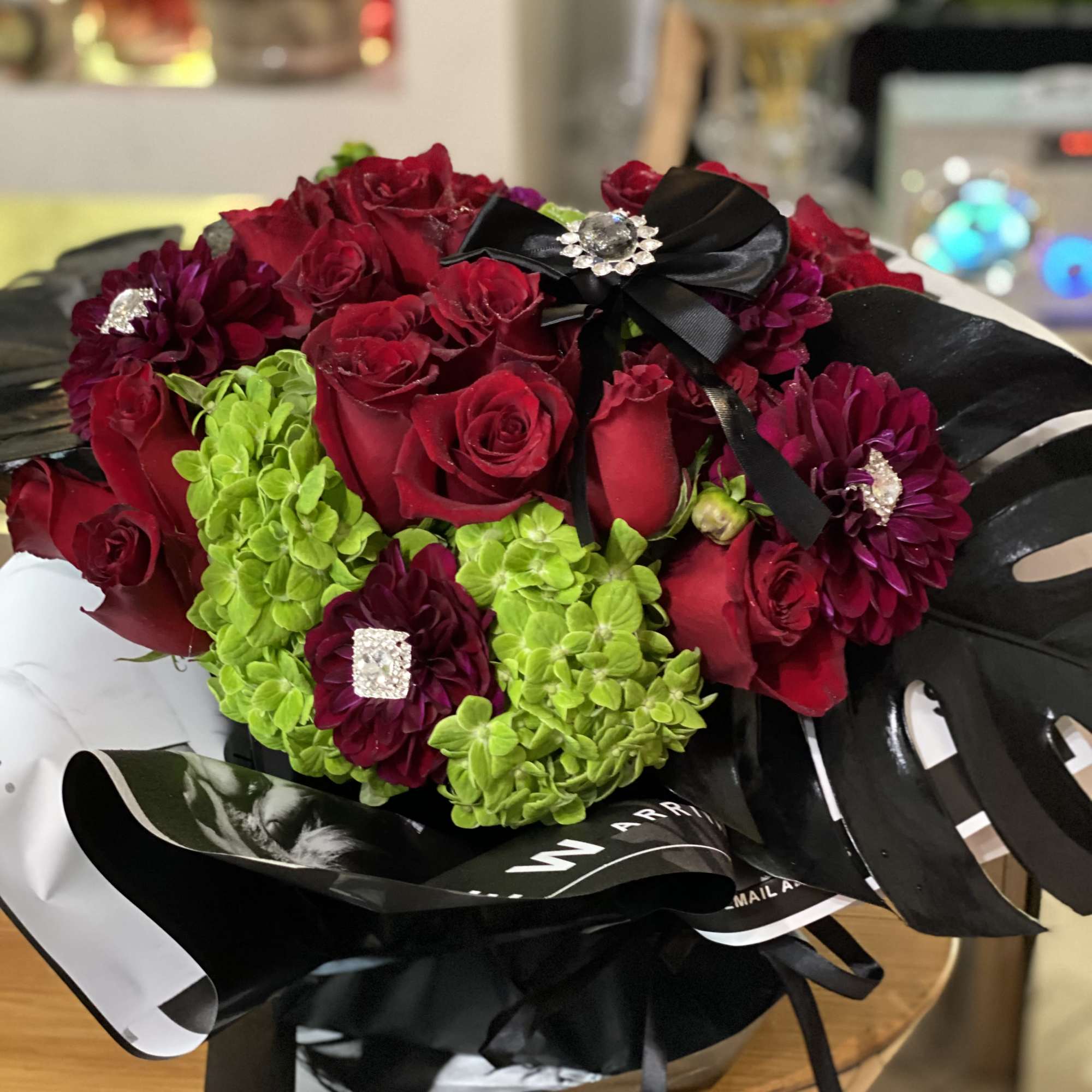 Wrapped, black, square vase flowing with luscious, red roses. Surrounded with black