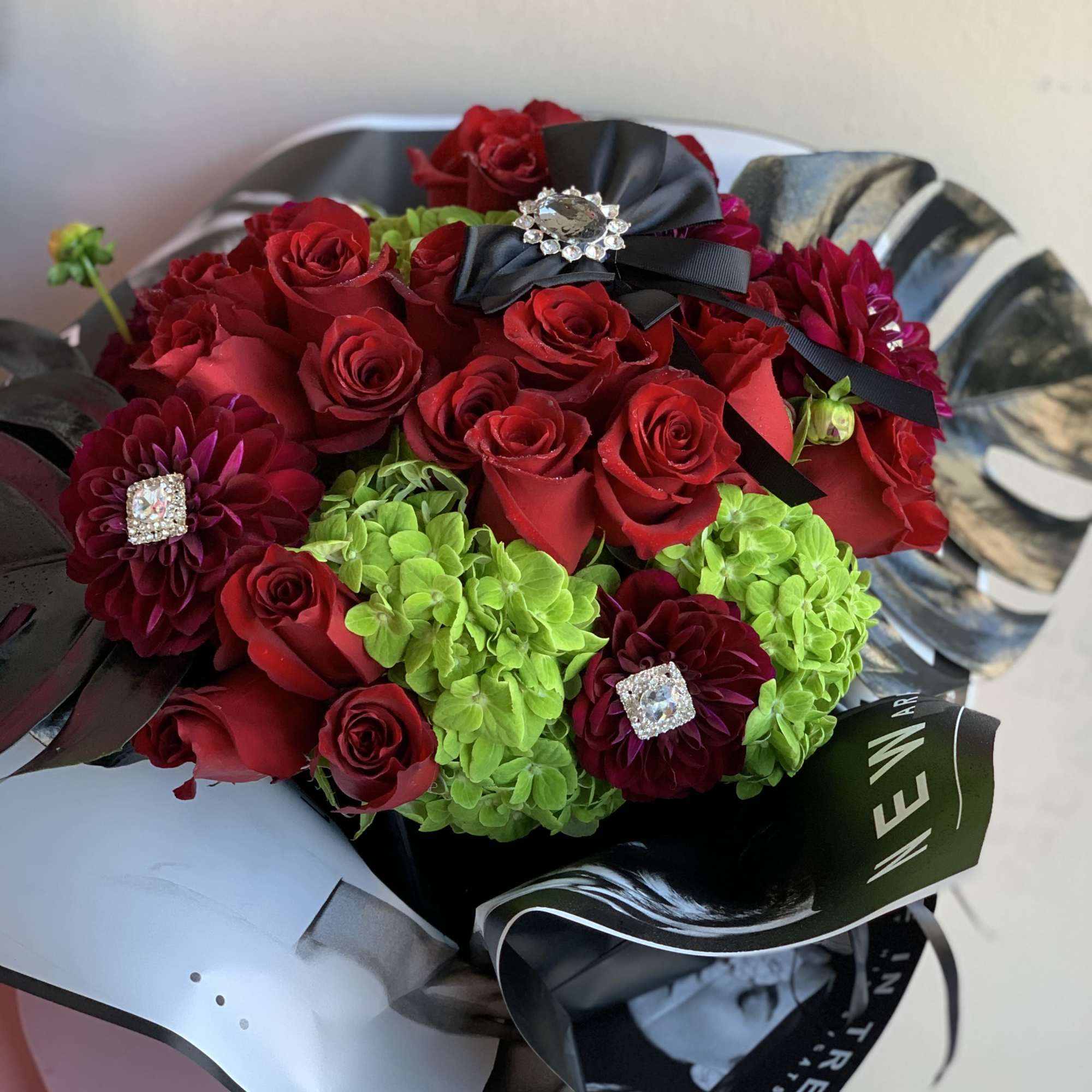 Wrapped, black, square vase flowing with luscious, red roses. Surrounded with black