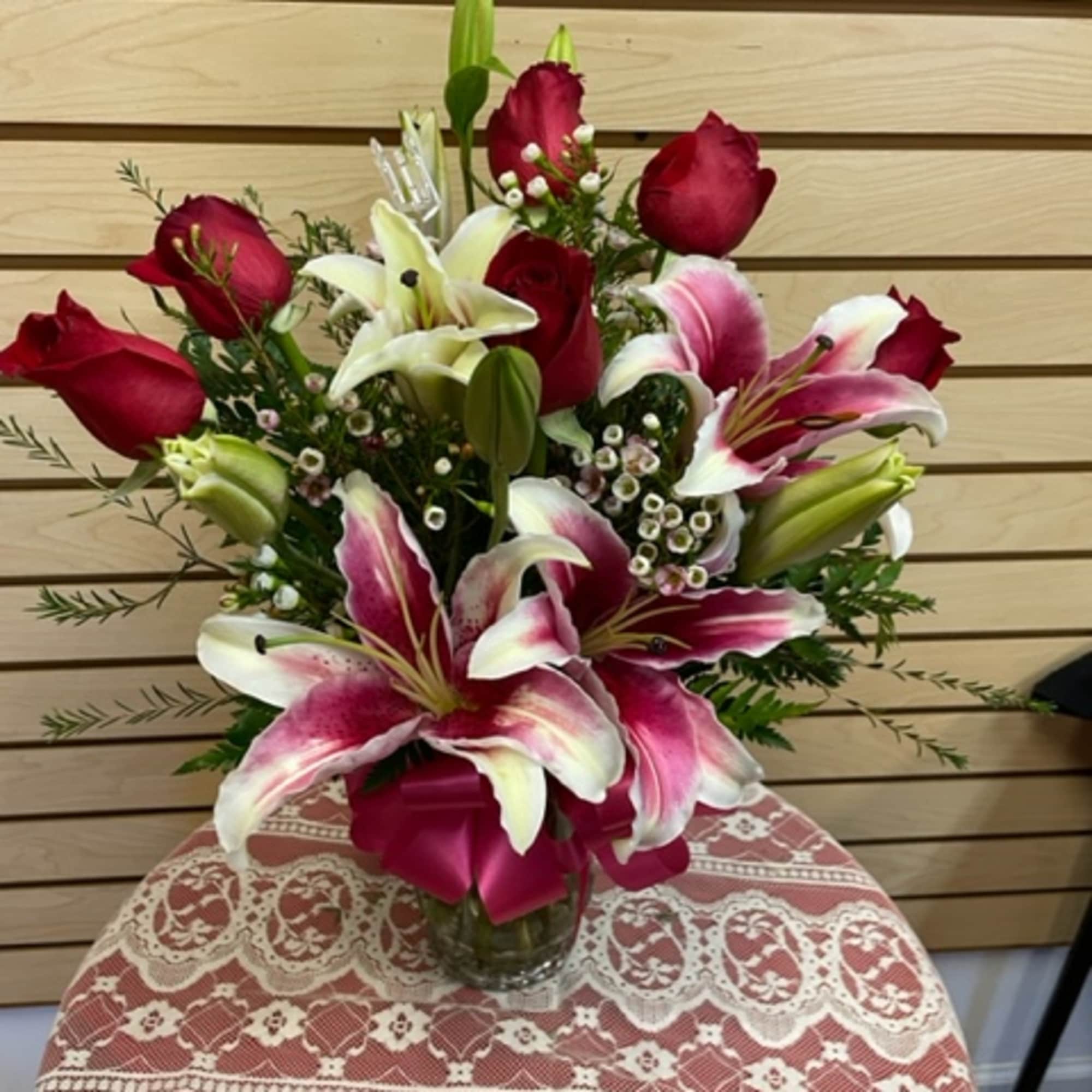 Mixed arrangement with red roses, stargazer lilies, and wax flowers in a Mixed arrangement with red roses, stargazer lilies, and wax flowers in a