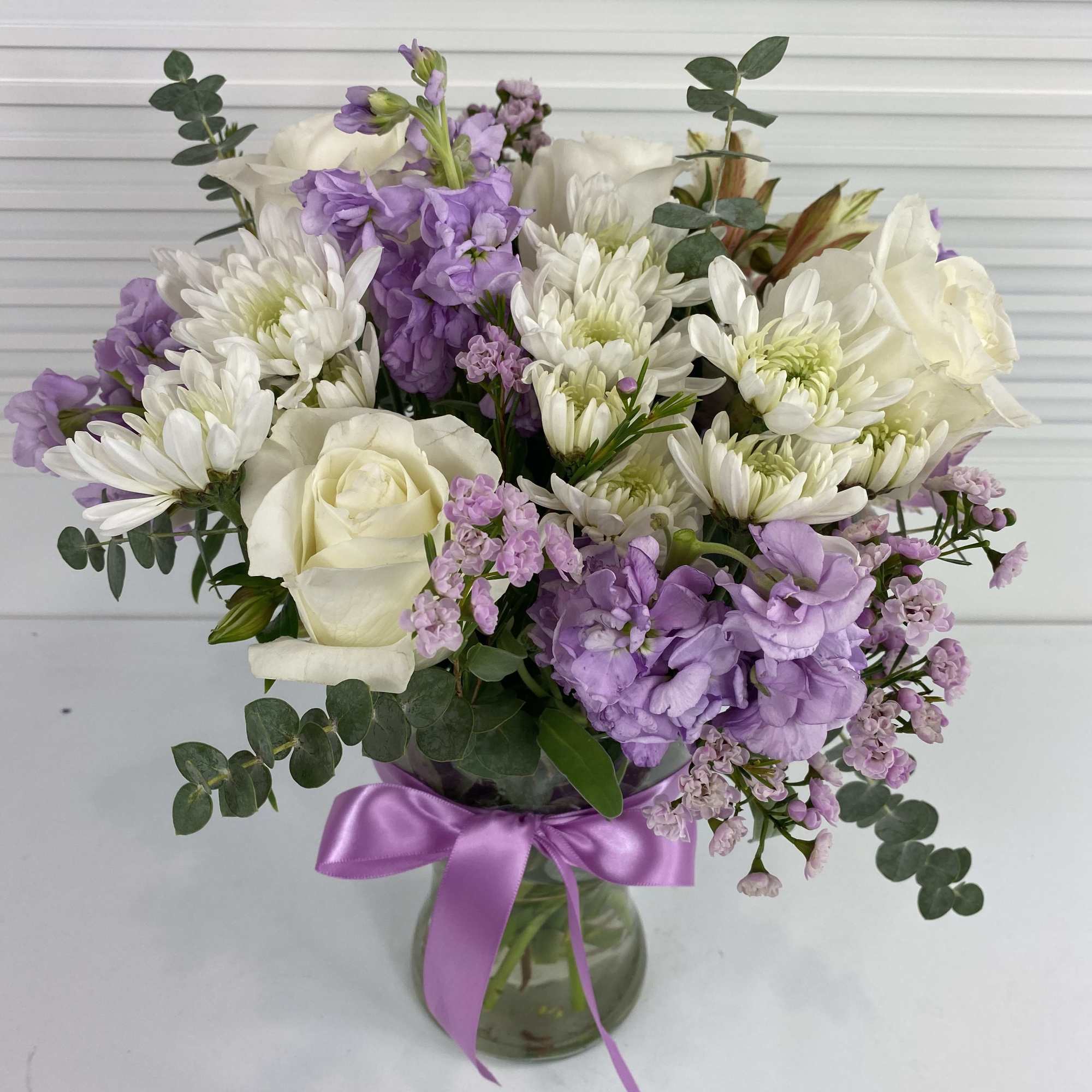 White roses, stocks, wax flower, daisies, alstroemerias and eucalyptus in a clear
