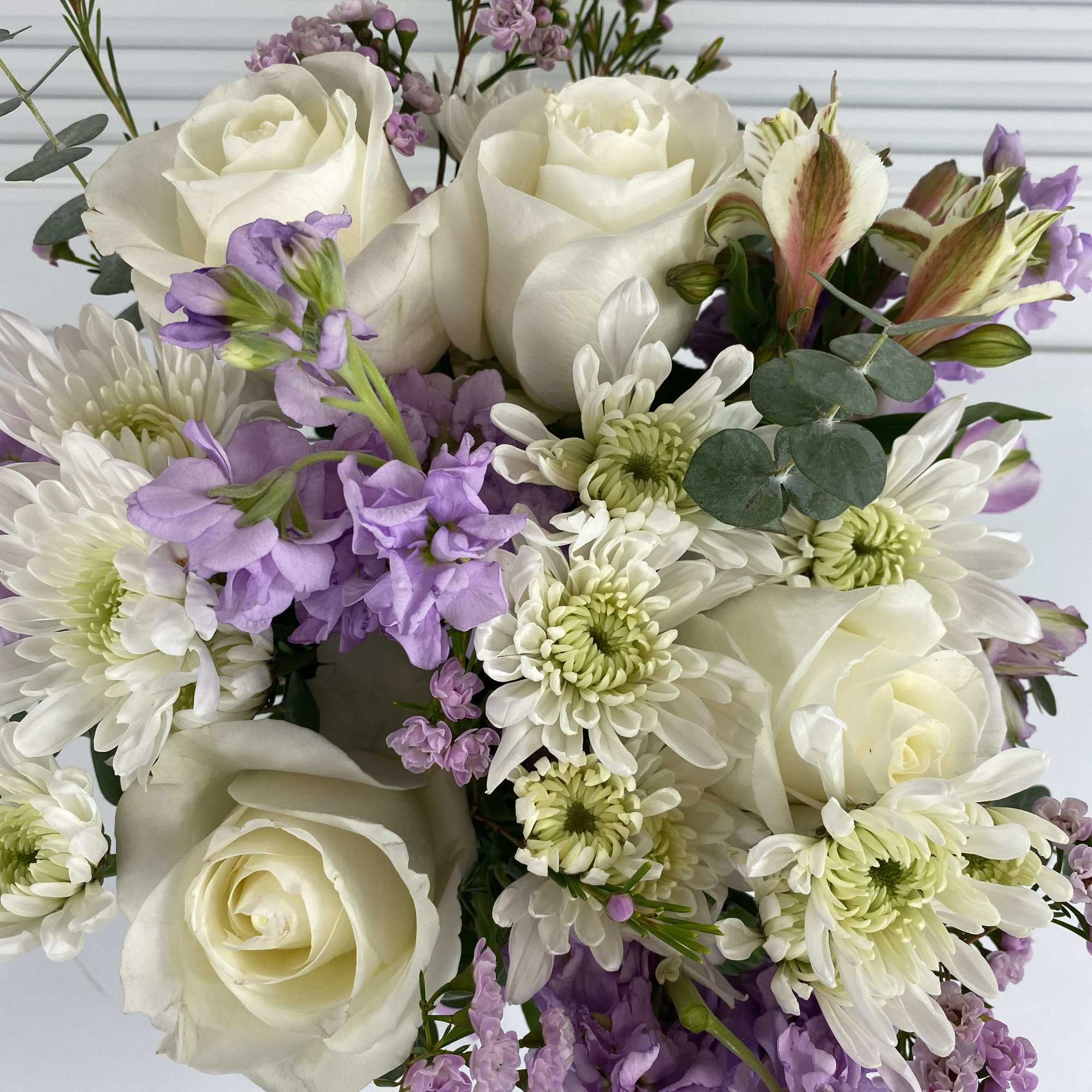White roses, stocks, wax flower, daisies, alstroemerias and eucalyptus in a clear