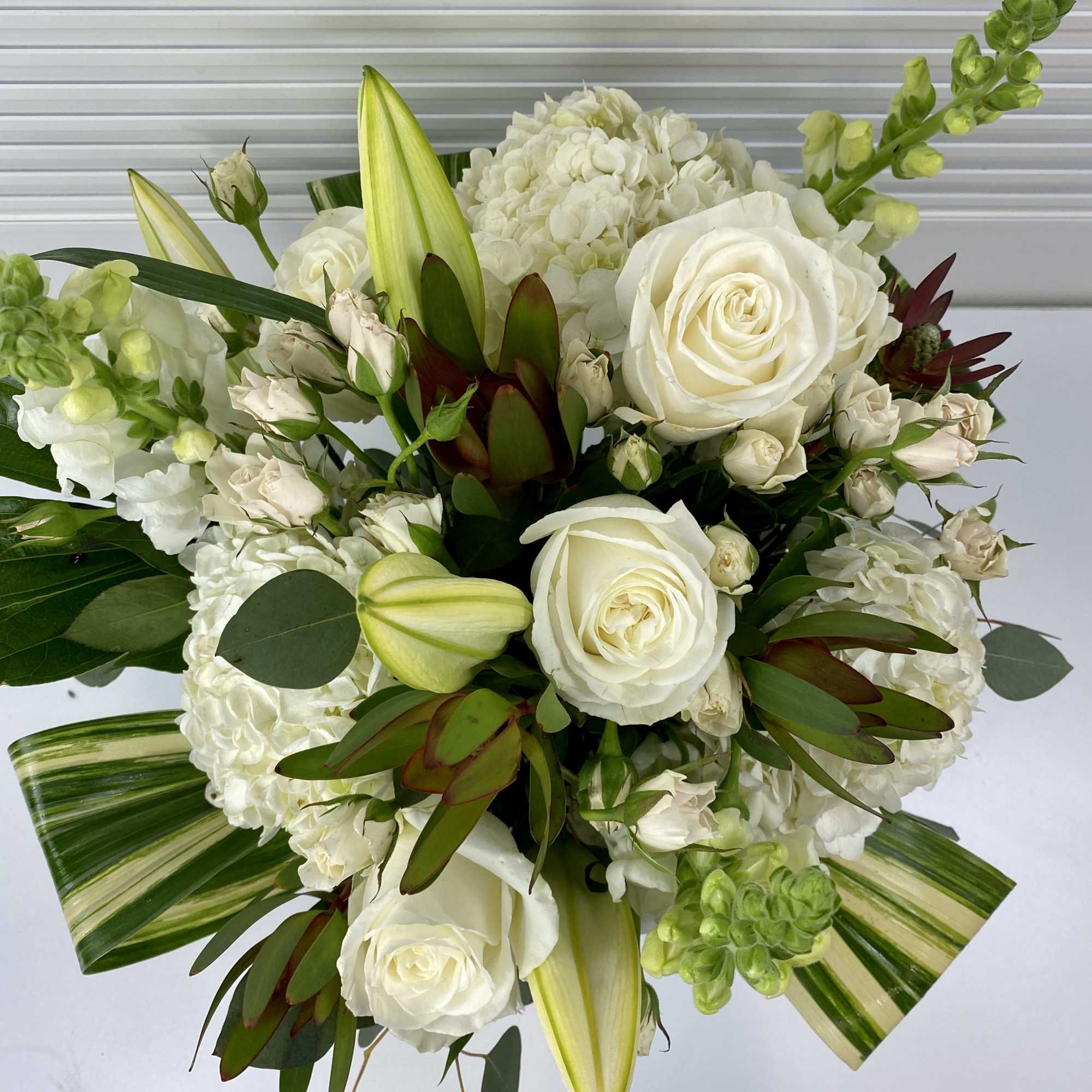 Green and white arrangement in a wooden vase. Hydrangeas, snapdragon, roses and