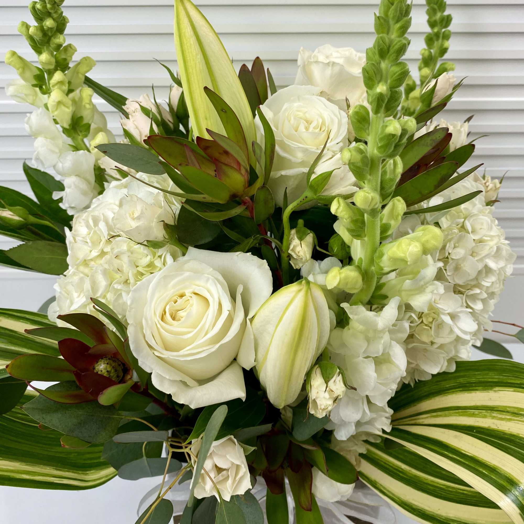 Green and white arrangement in a wooden vase. Hydrangeas, snapdragon, roses and