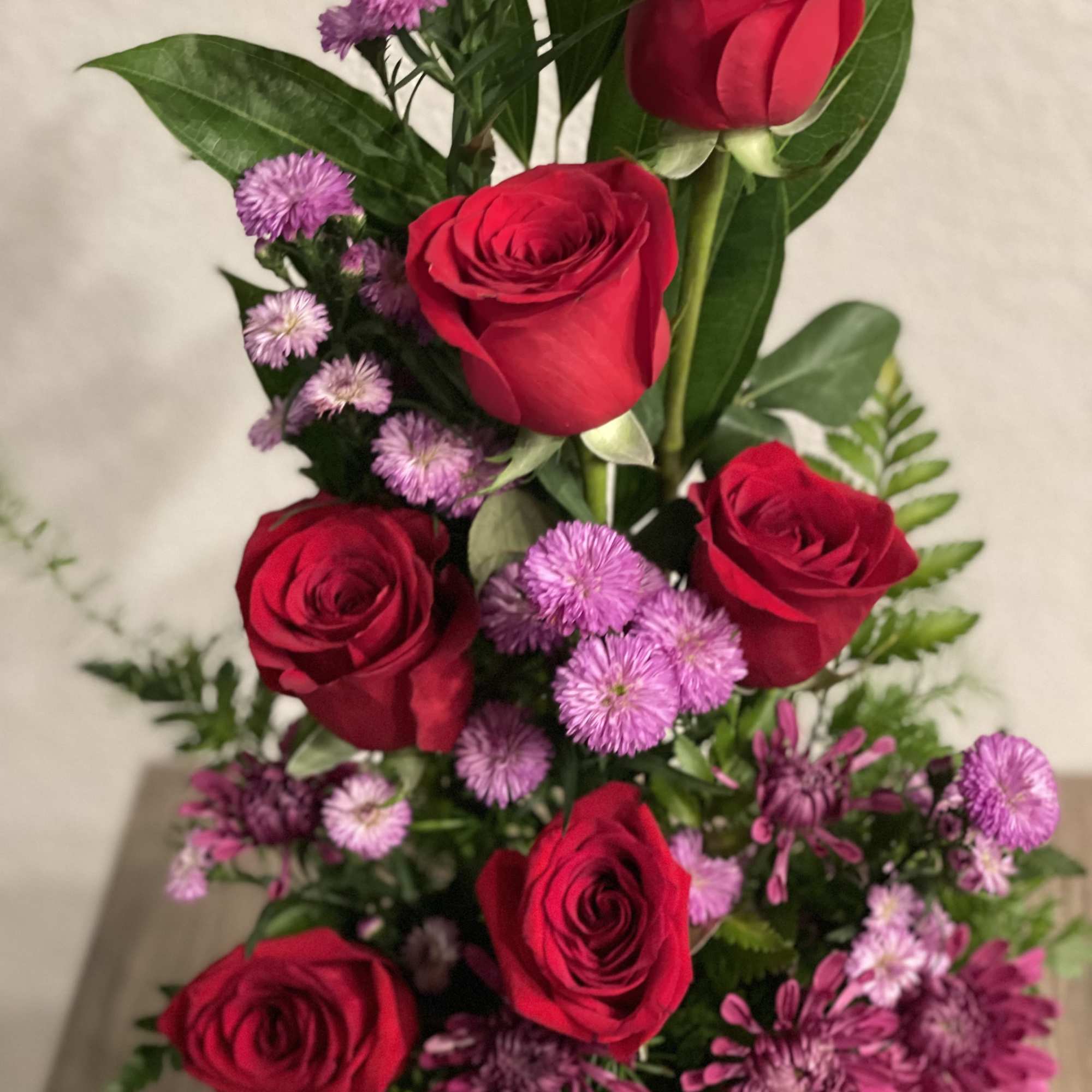 Beautiful form arrangement of red roses, dark pink aster flowers,, mums and