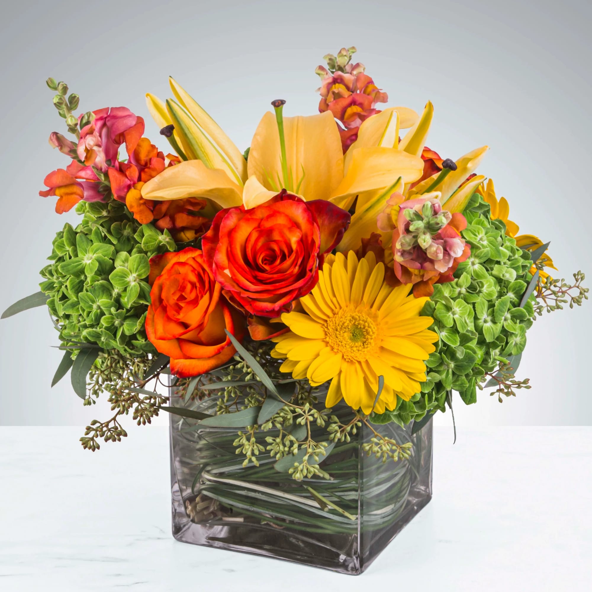 This bright yellow, green, and orange arrangement includes roses, daisies, and lilies