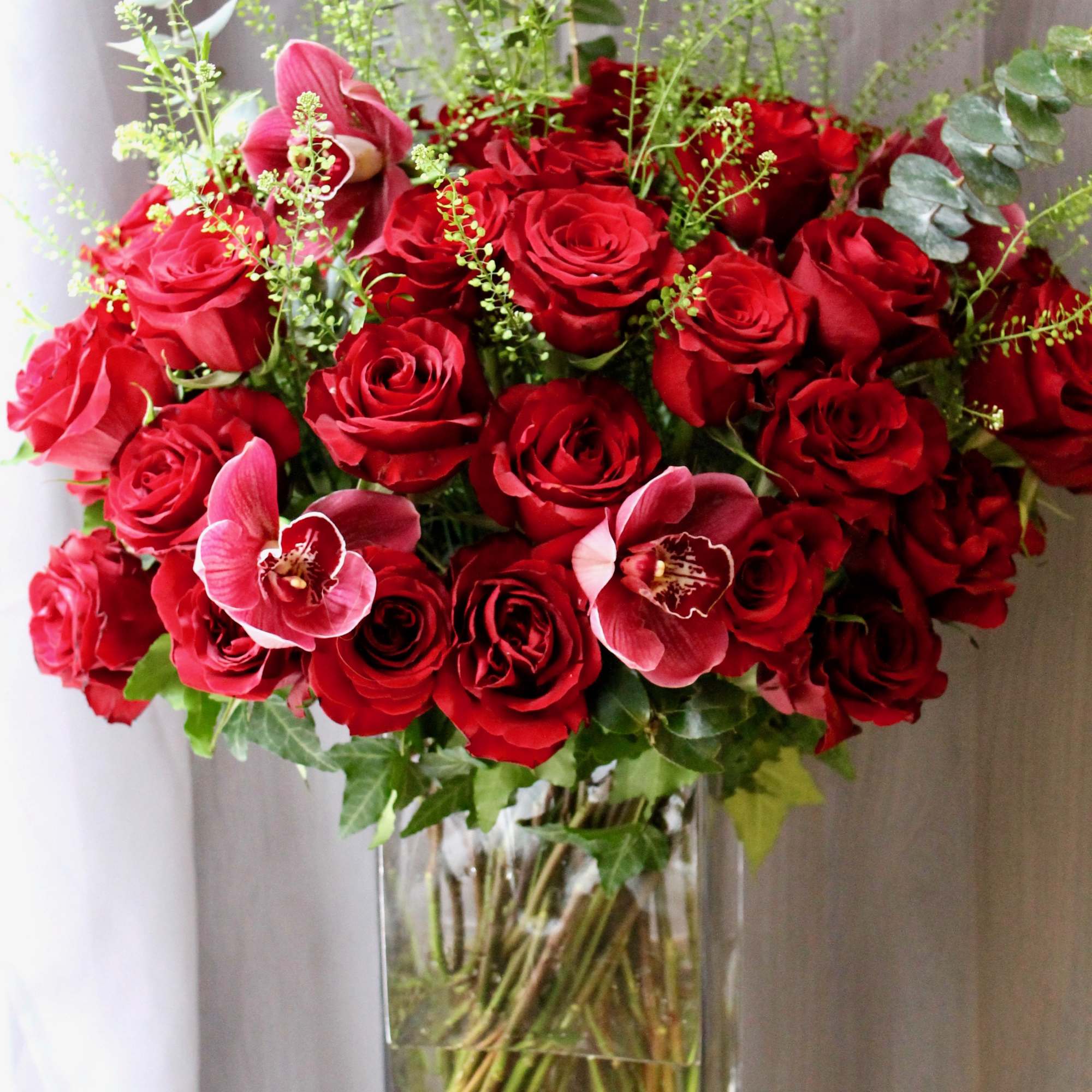 Gorgeous red long stem roses with ivy, orchids and pretty greenery. Send