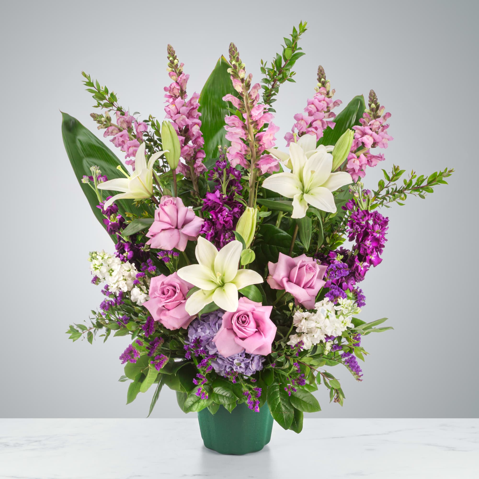 A purple and white sympathy basket featuring snapdragons, roses, lilies, and stock.
