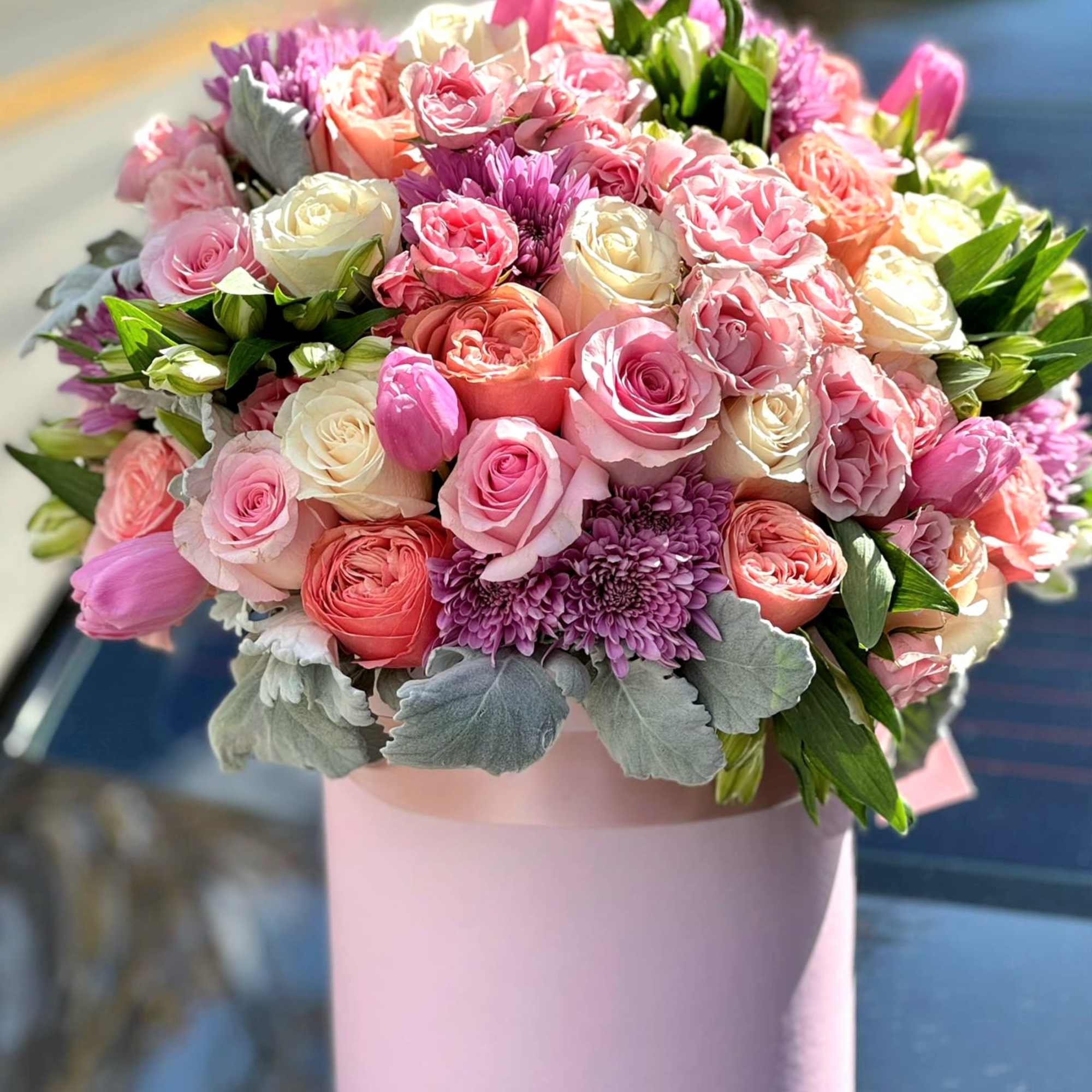 This luxury hatbox arrangement features premium roses, tulips, and ranunculus in soft