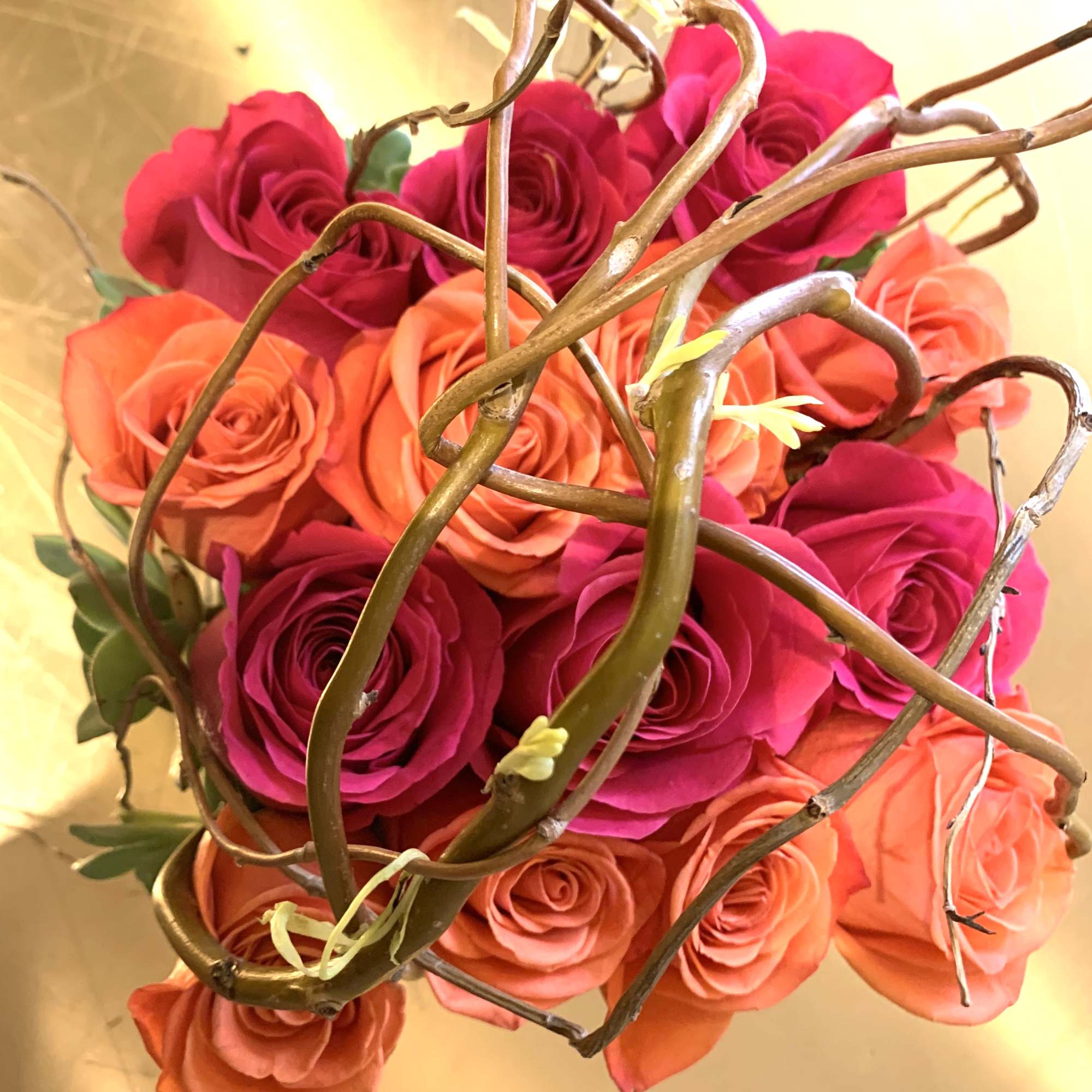 Coral roses, accented with curly willow in a gorgeous golden ceramic vase.