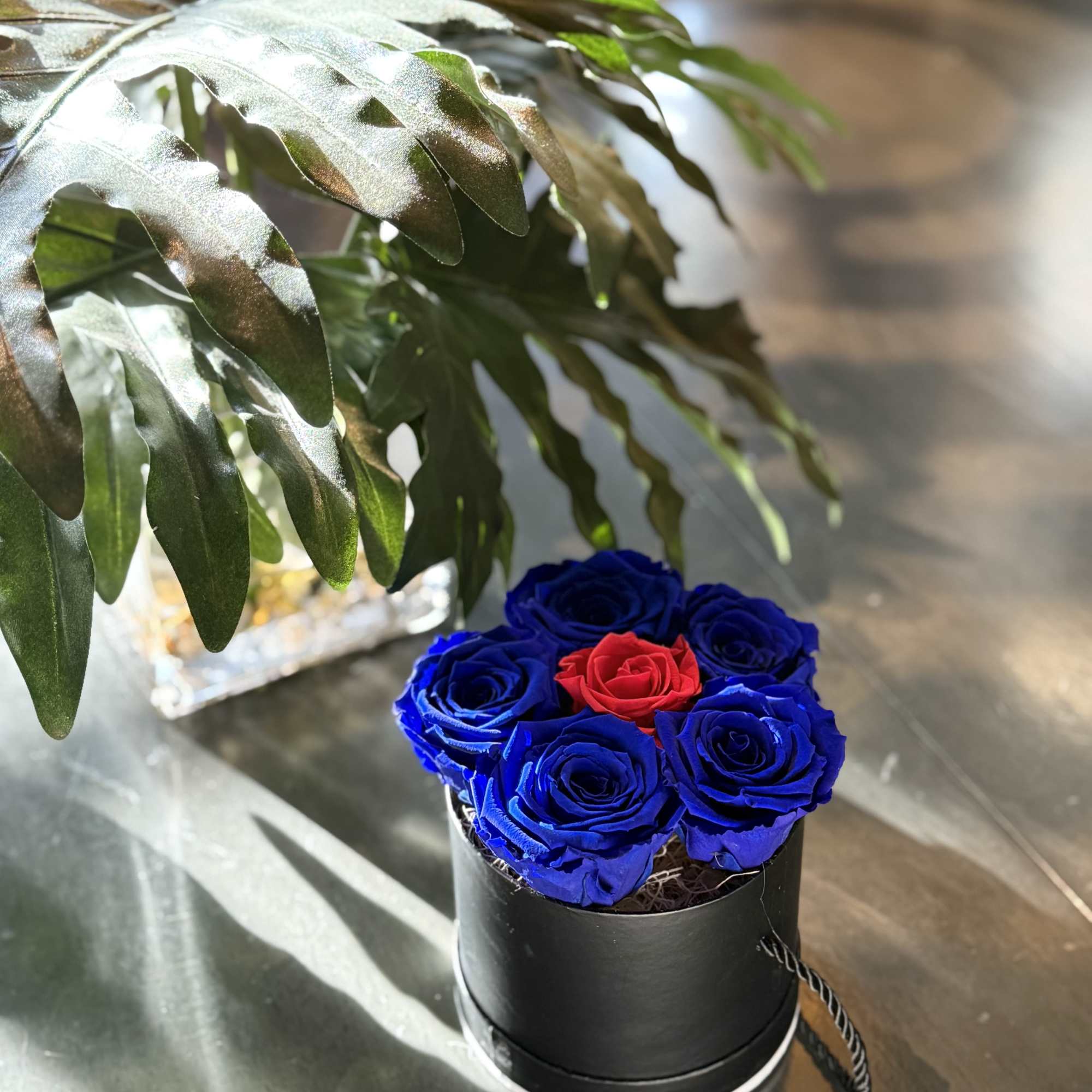 This striking round black floral box features five preserved blue roses on