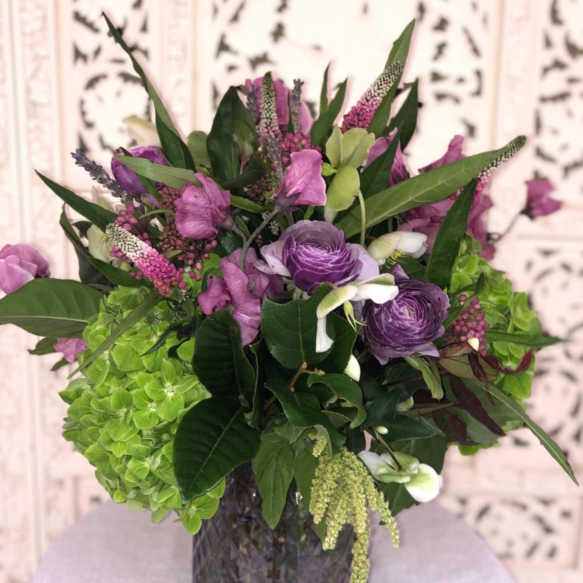 Lush assortment of purple flowers such as Ranunculus, Veronica, Sweet Pea and