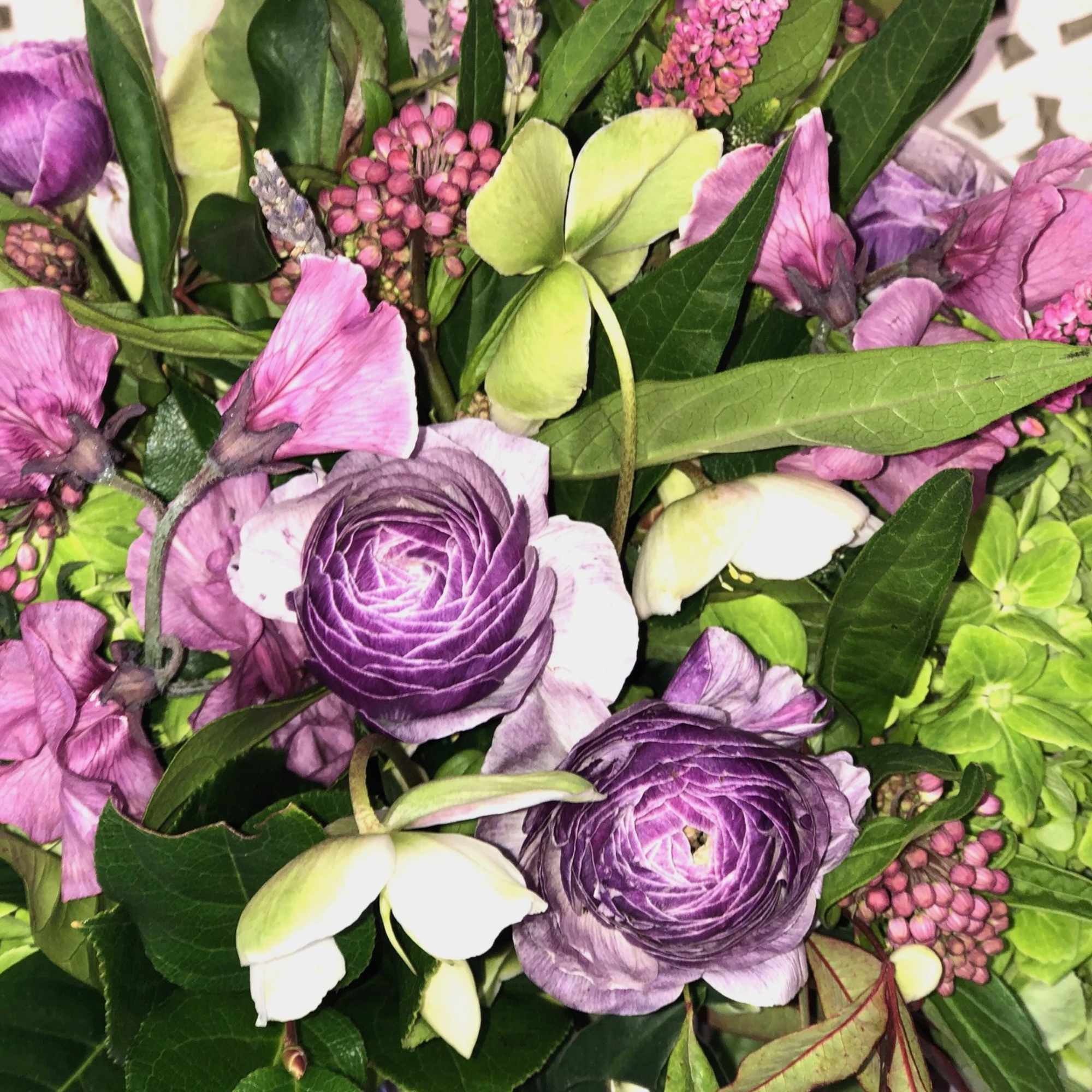 Lush assortment of purple flowers such as Ranunculus, Veronica, Sweet Pea and