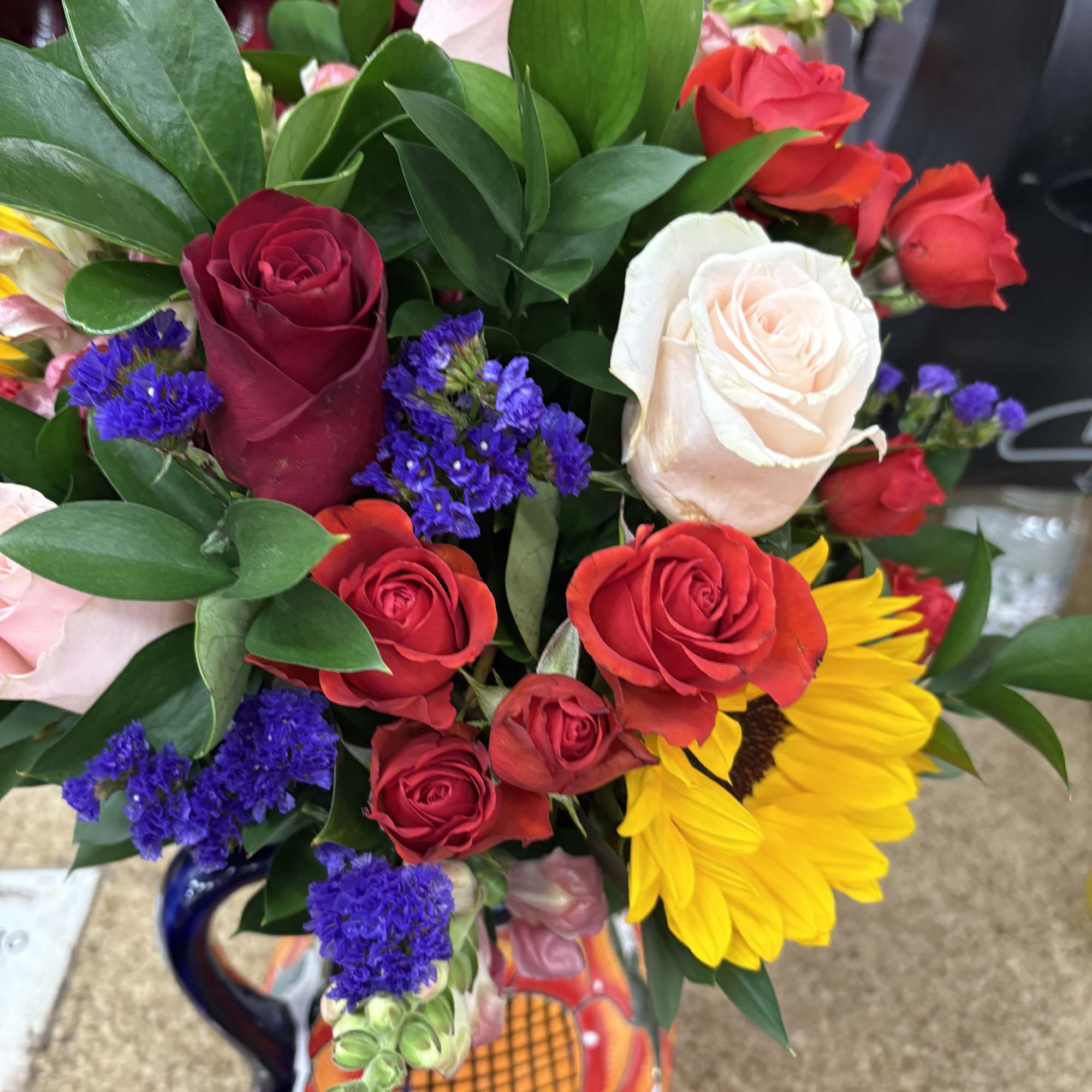 Mini roses, roses, sunflowers, statice and greenery in an artisan pitcher making