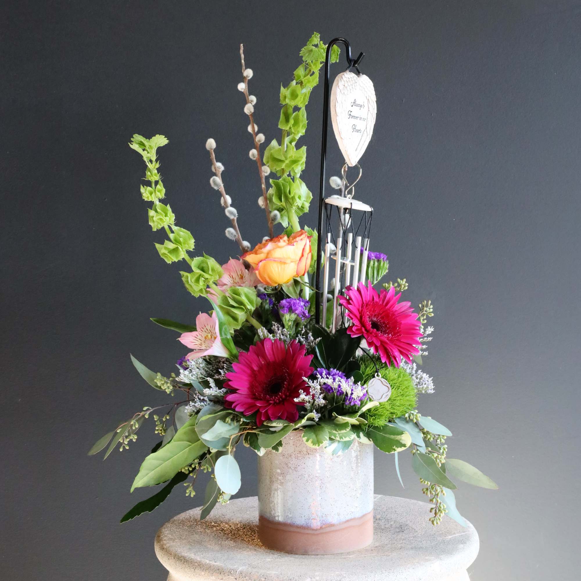 A gorgeous sympathy arrangement with a small hanging wind chime keepsake with