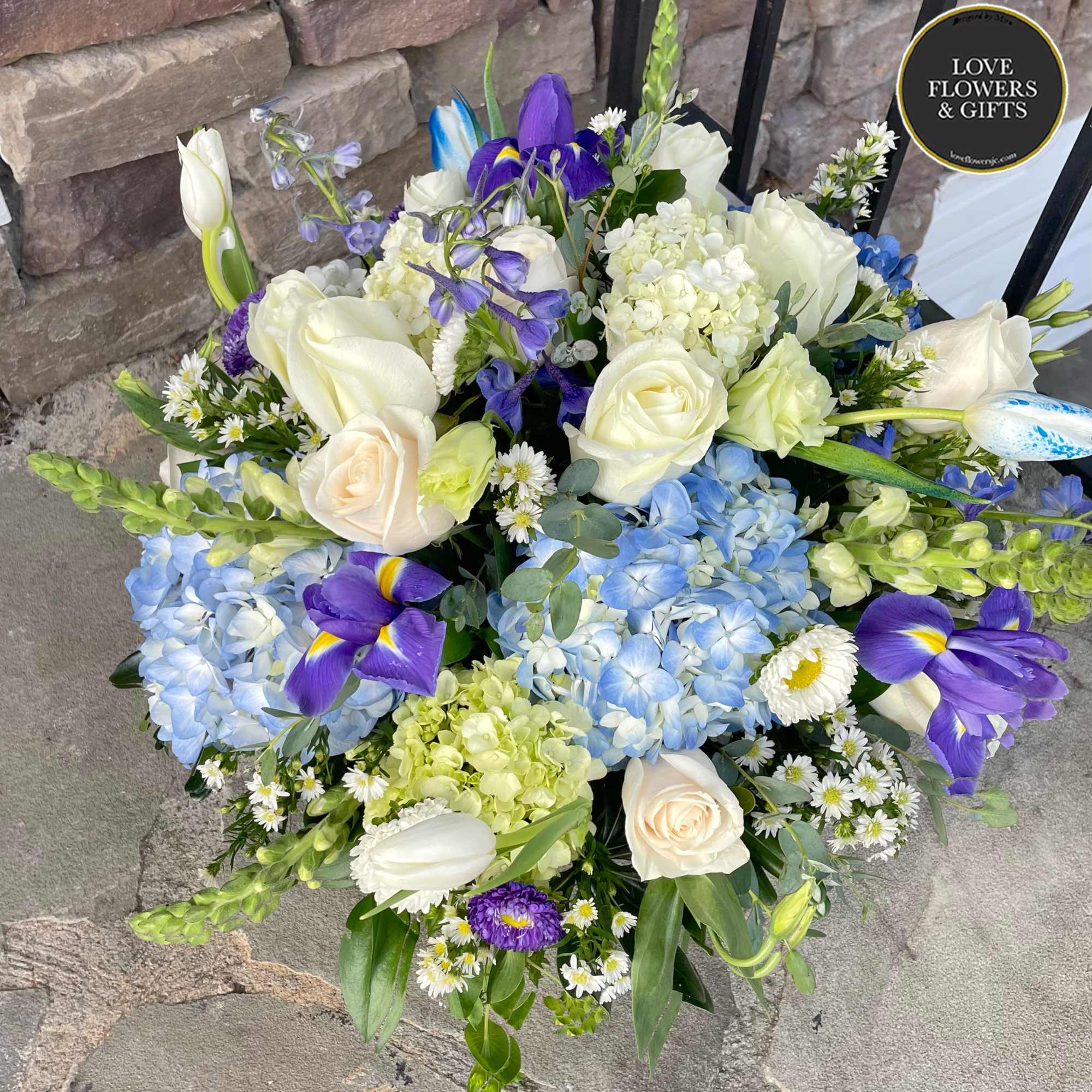 A large centerpiece made of blues and whites of roses, hydrangeas, iris