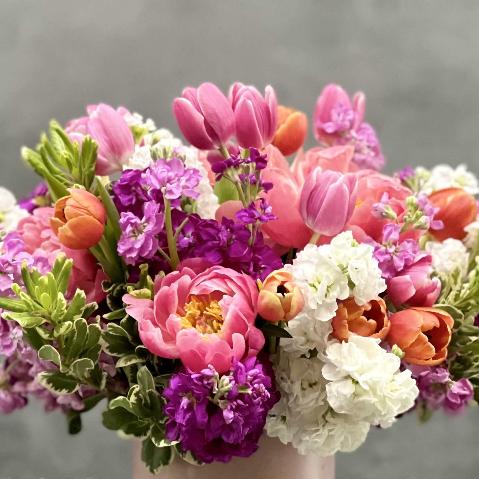 Lush tones of pink, orange and lavender seasonal blooms which includes peonies