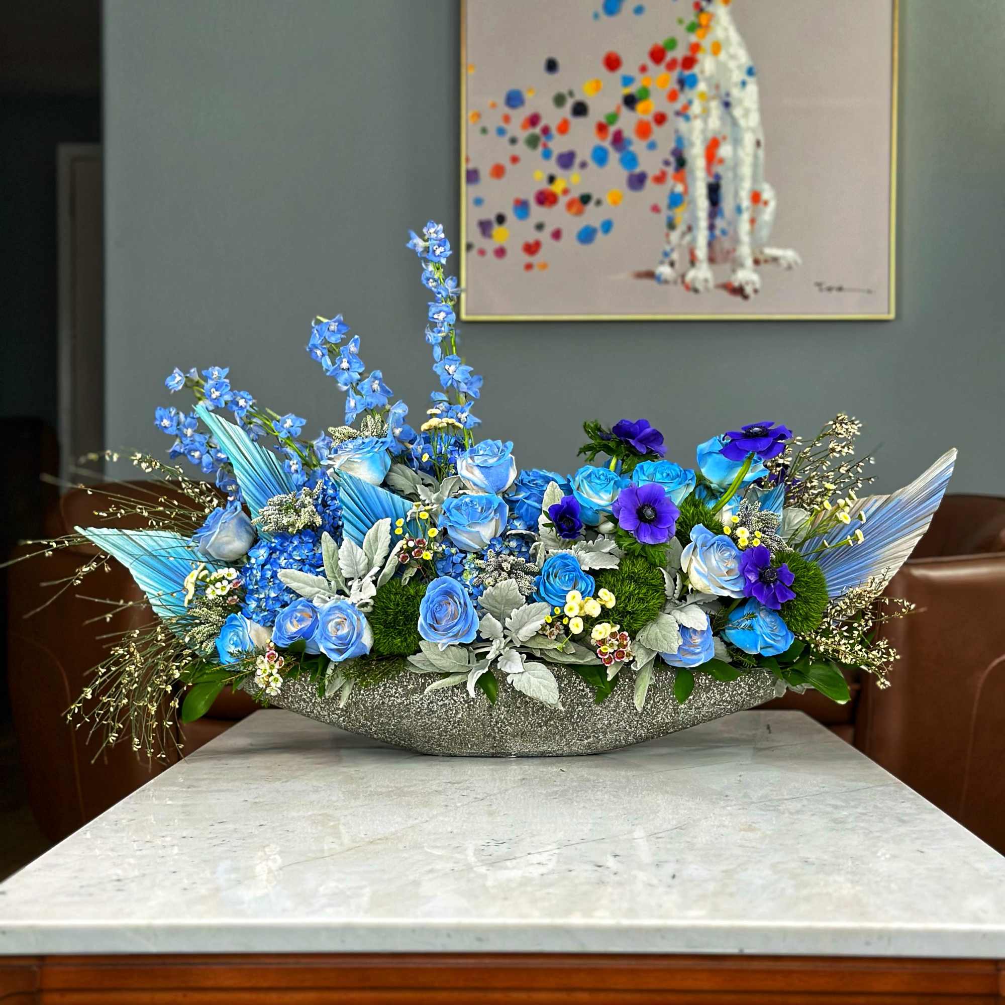 A stunning centerpiece featuring vibrant blue roses, delicate anemones, and lush greenery