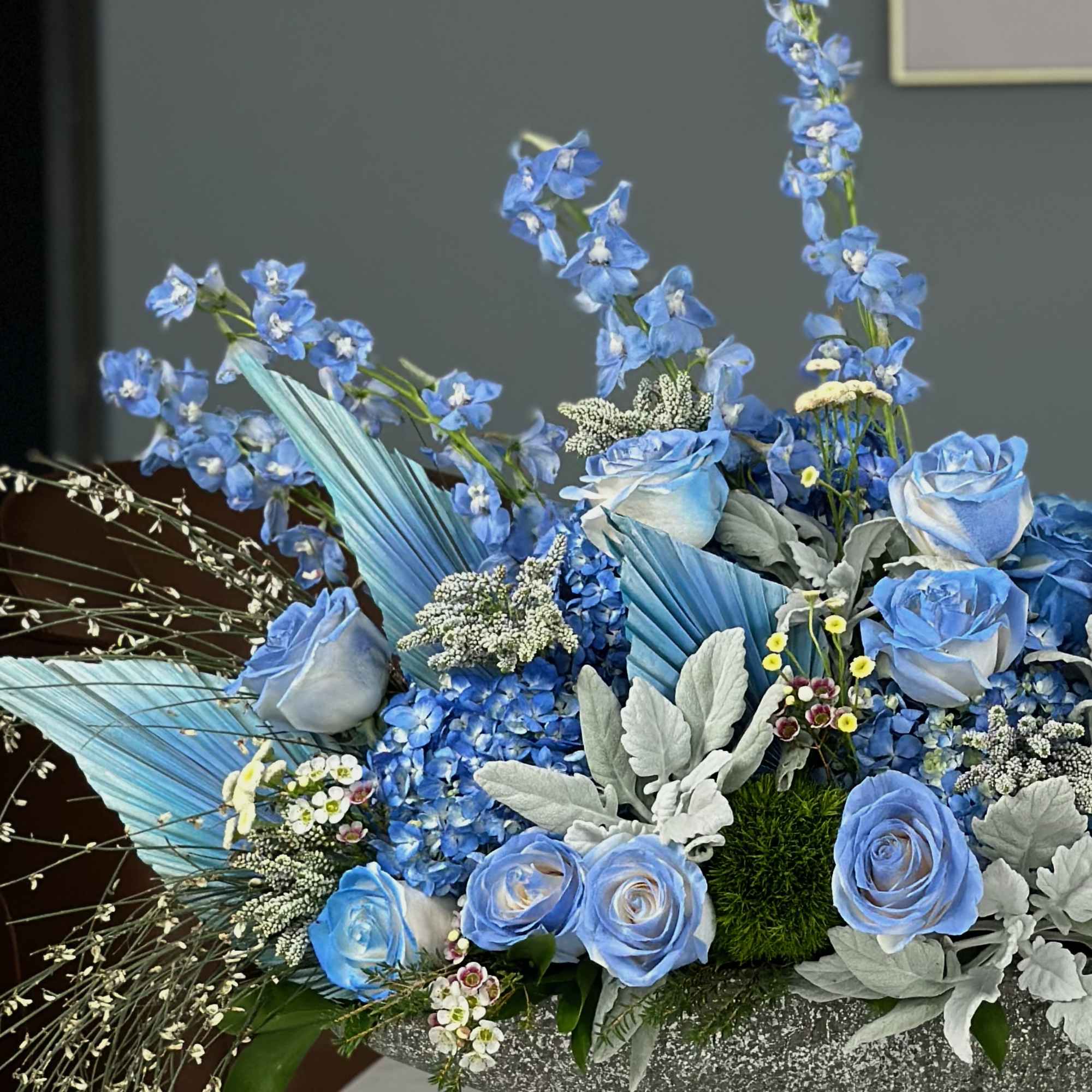 A stunning centerpiece featuring vibrant blue roses, delicate anemones, and lush greenery