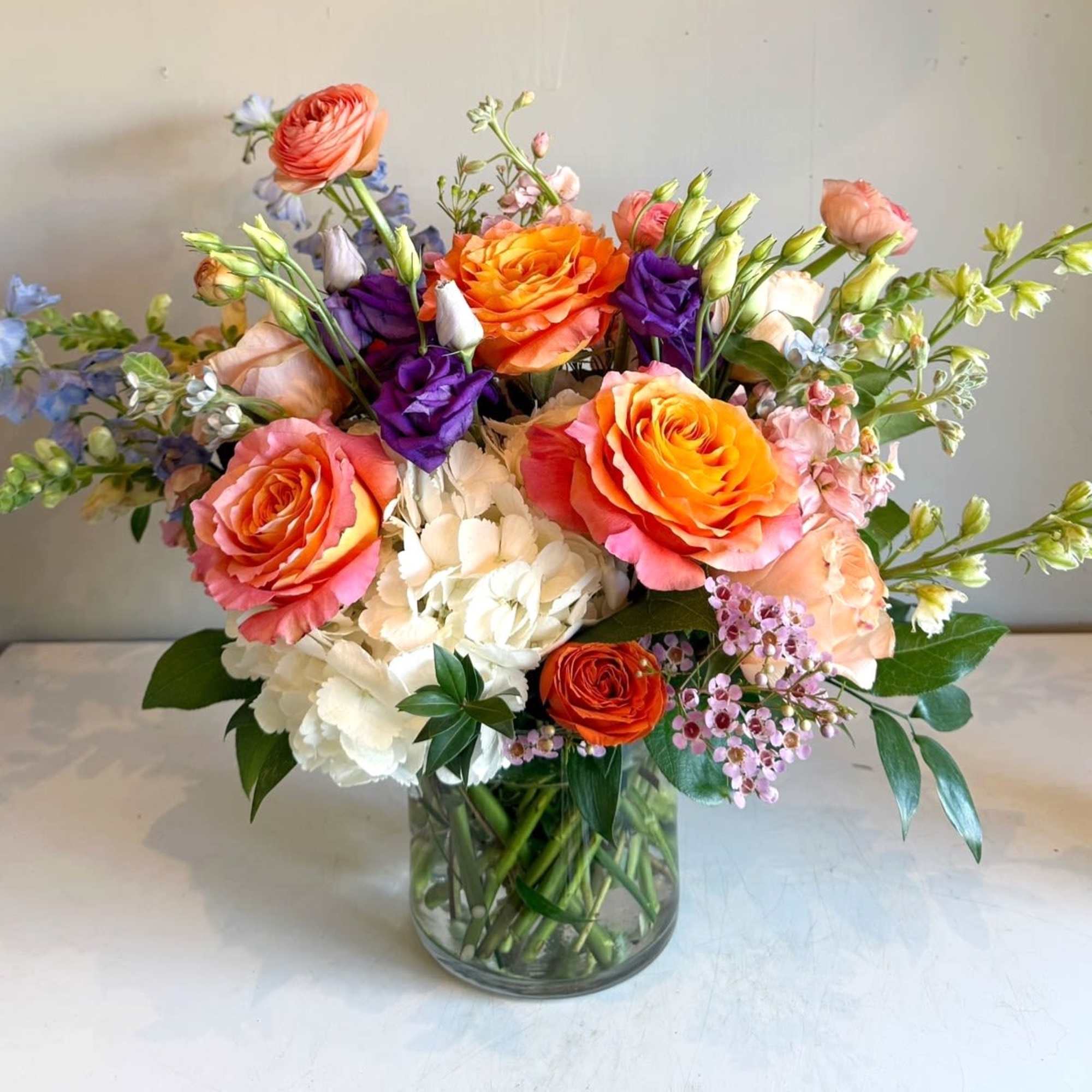 This stunning arrangement combines the fiery zest of orange, pops of purple This stunning arrangement combines the fiery zest of orange, pops of purple