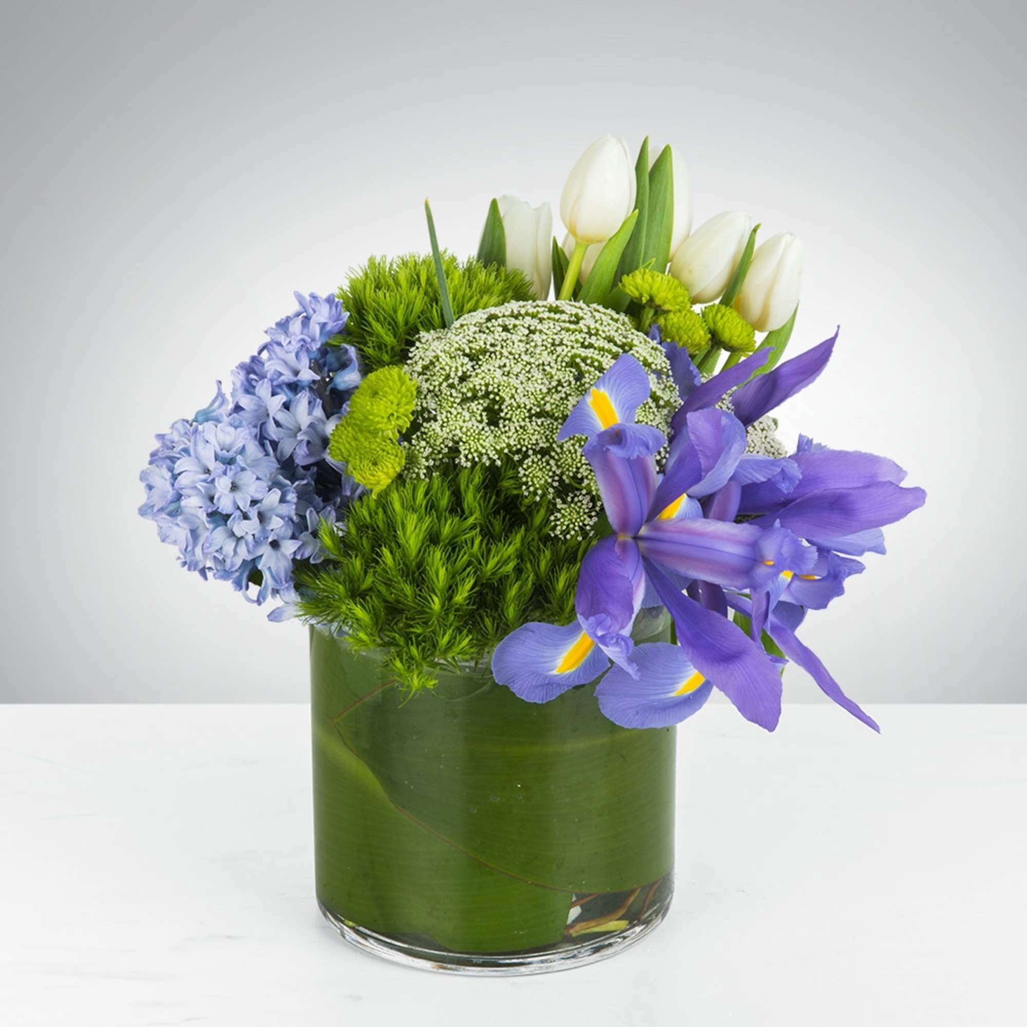 This arrangement includes flowers like green dianthus, blue iris, white tulips, hyacinths This arrangement includes flowers like green dianthus, blue iris, white tulips, hyacinths
