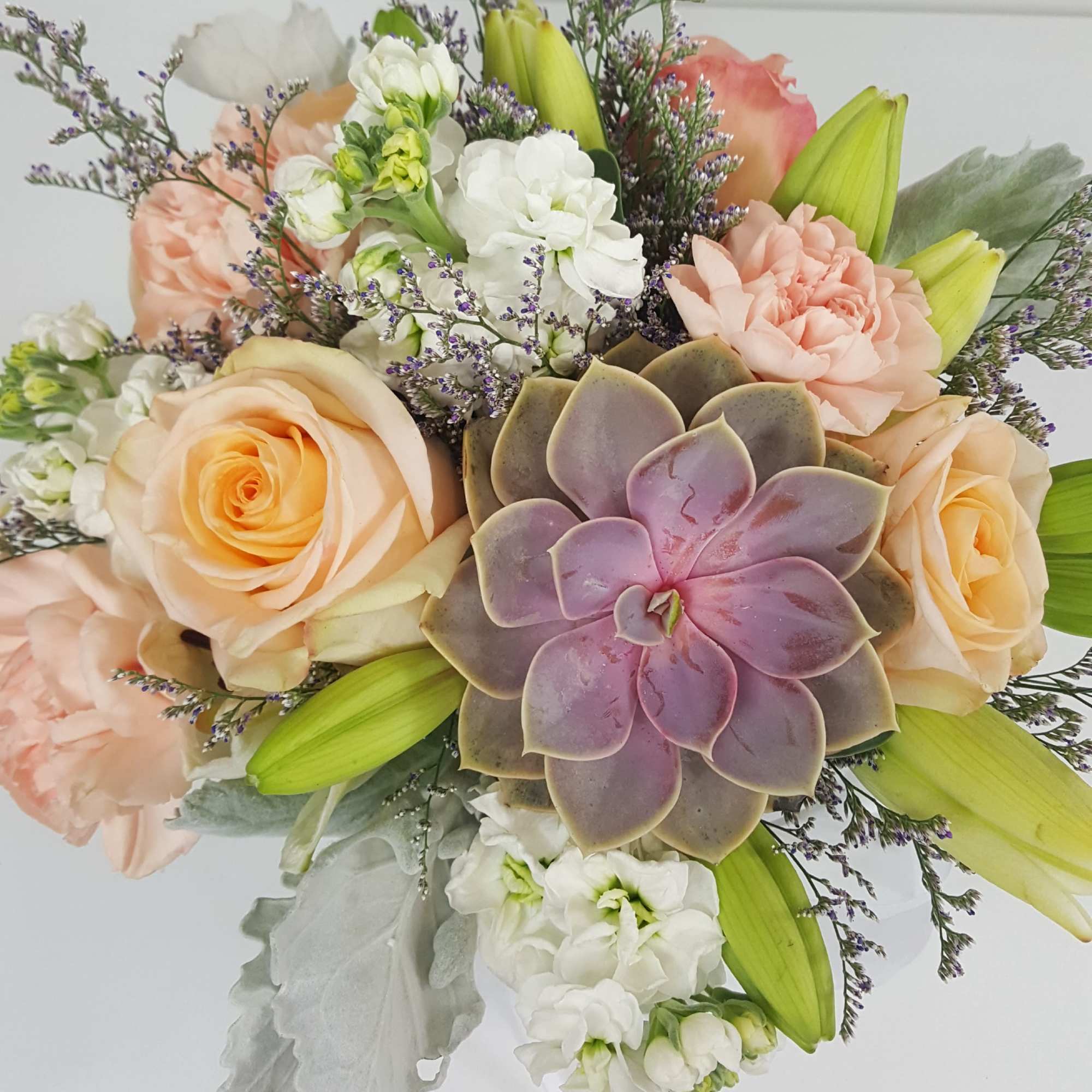 White lilies, roses, stocks, succulent and fillers in a clear rectangular vase
