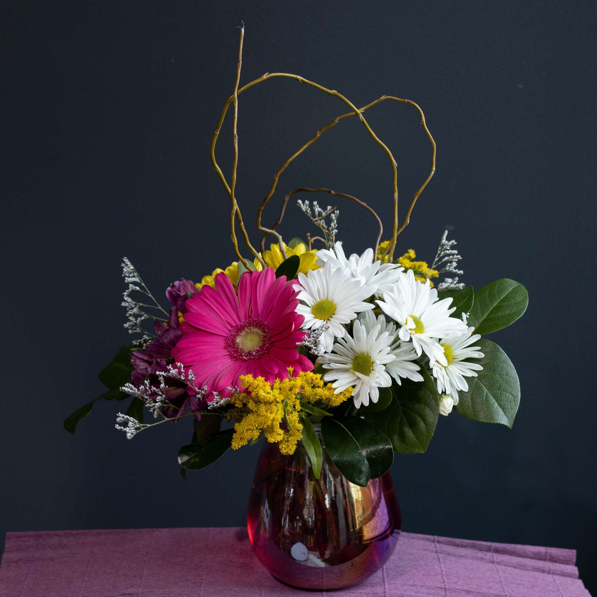 A fun playful arrangement filled with a variety of daisies and other