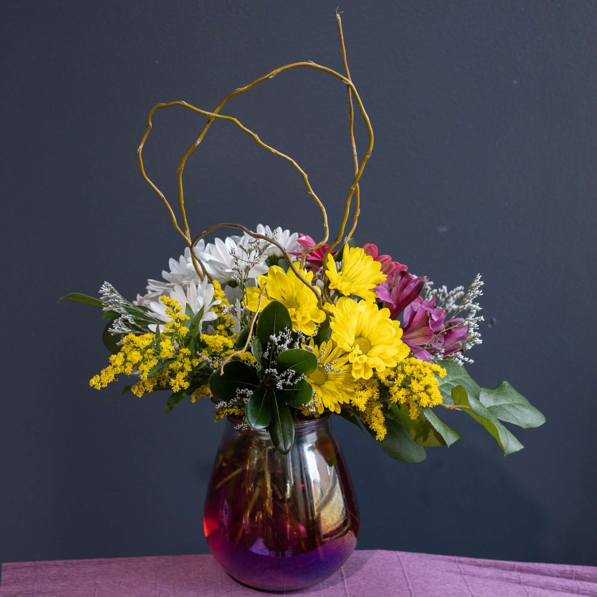 A fun playful arrangement filled with a variety of daisies and other