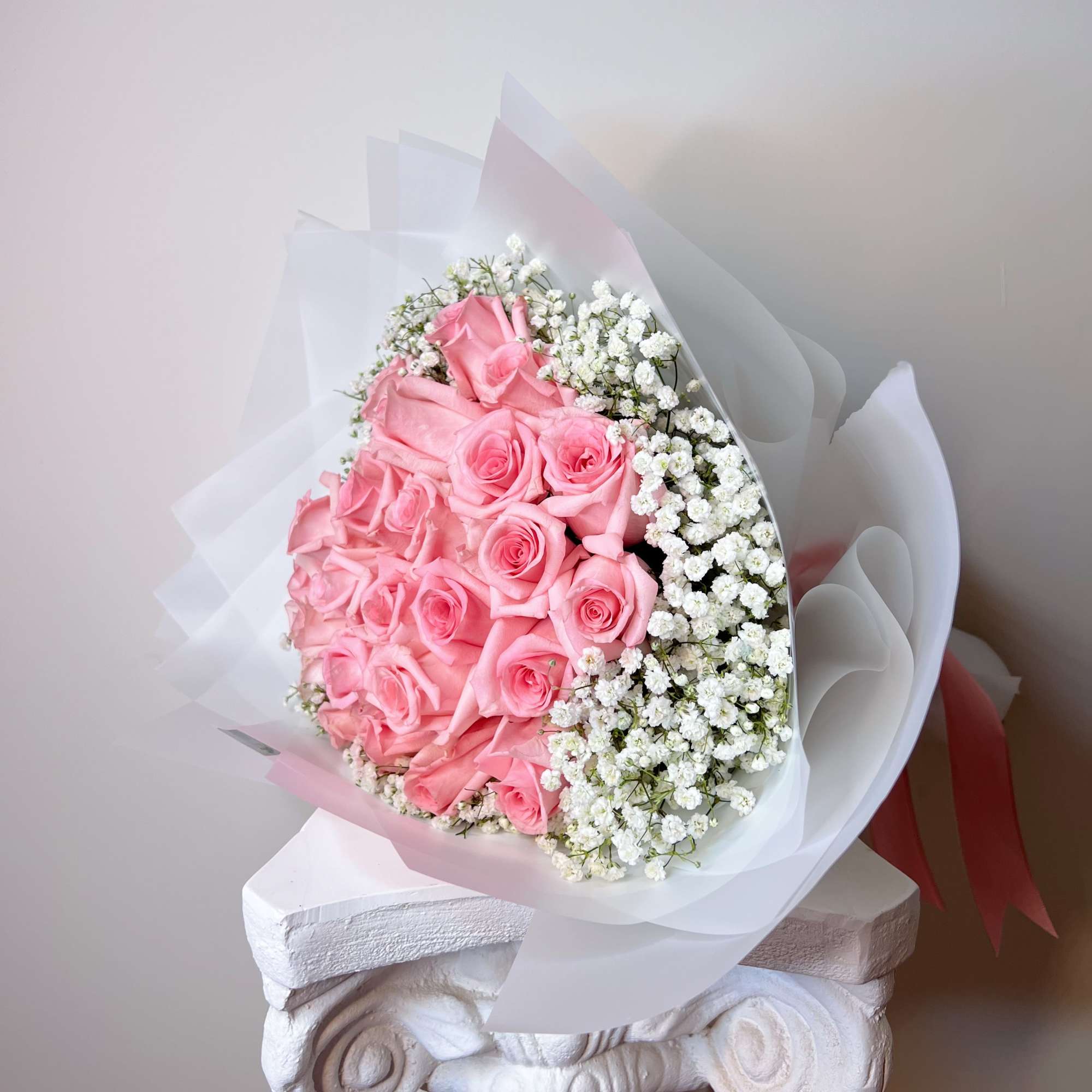 A bouquet of pink roses paired with gypsophila, wrapped in white paper.