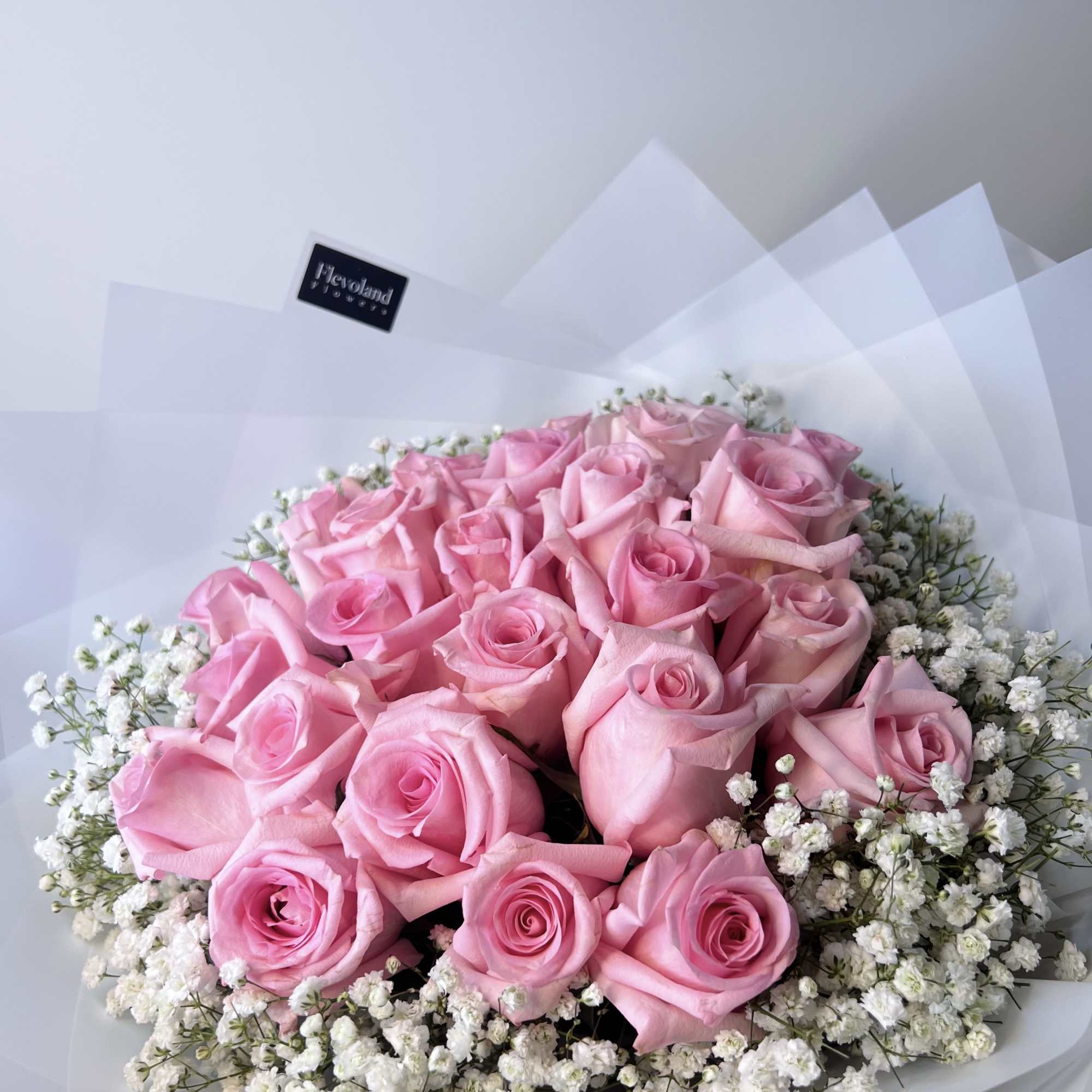 A bouquet of pink roses paired with gypsophila, wrapped in white paper.